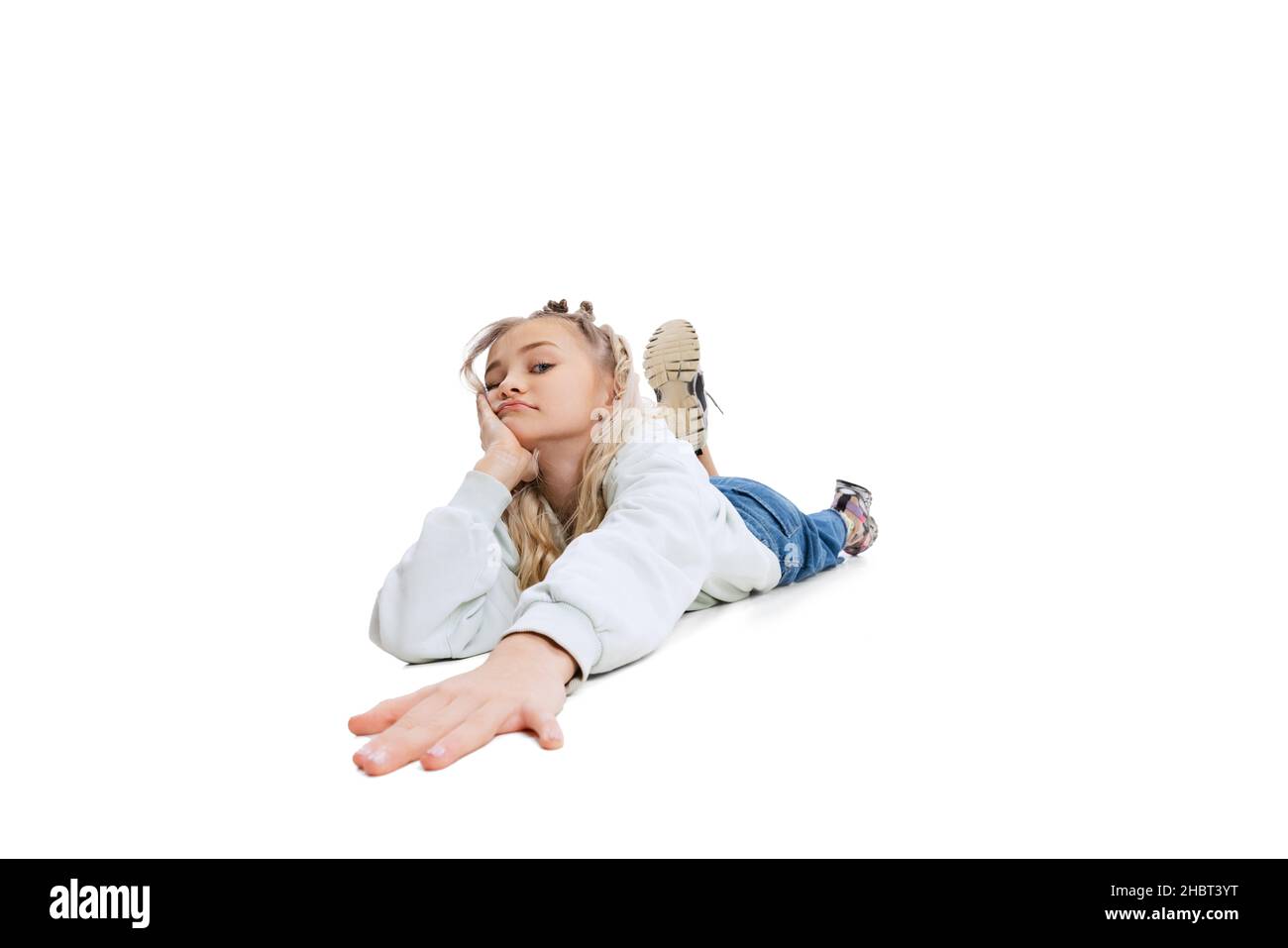 Bonita niña pequeña, niño aburrido en ropa informal tumbado en el suelo aislado en el fondo blanco del estudio. Emociones Foto de stock