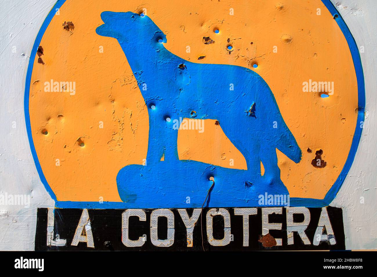 Agujeros de bala en una placa de acero con un coyote azul en un círculo amarillo con la leyenda La Coyotera en un ejido, rancho y rancheria en la carretera Alcar, Caborca y Puerto Peñasco en el Desierto de Sonora. Crimen organizado, violencia, armas, Cartel. © (© Foto: LuisGutierrez / NortePhoto.com) © Agujeros de balas en letrero de lámina de acero con un coyote azul en un curculo amarillo con la leyenda La Coyotera en un ejido, rancho y rancheria en la carretera Alcar, Caborca y Puerto Peñasco en el Desierto de Sonora. Crimen organizado, violencia, Cararmtel. © (© Foto: LuisGutiérrez/Norte Foto de stock