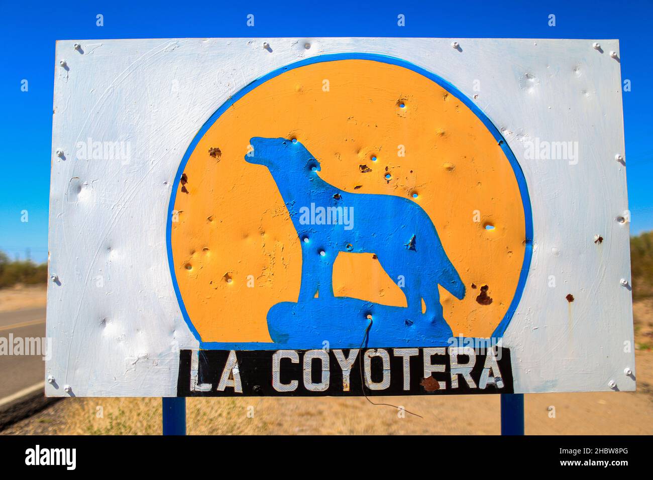 Agujeros de bala en una placa de acero con un coyote azul en un círculo amarillo con la leyenda La Coyotera en un ejido, rancho y rancheria en la carretera Alcar, Caborca y Puerto Peñasco en el Desierto de Sonora. Crimen organizado, violencia, armas, Cartel. © (© Foto: LuisGutierrez / NortePhoto.com) © Agujeros de balas en letrero de lámina de acero con un coyote azul en un curculo amarillo con la leyenda La Coyotera en un ejido, rancho y rancheria en la carretera Alcar, Caborca y Puerto Peñasco en el Desierto de Sonora. Crimen organizado, violencia, Cararmtel. © (© Foto: LuisGutiérrez/Norte Foto de stock