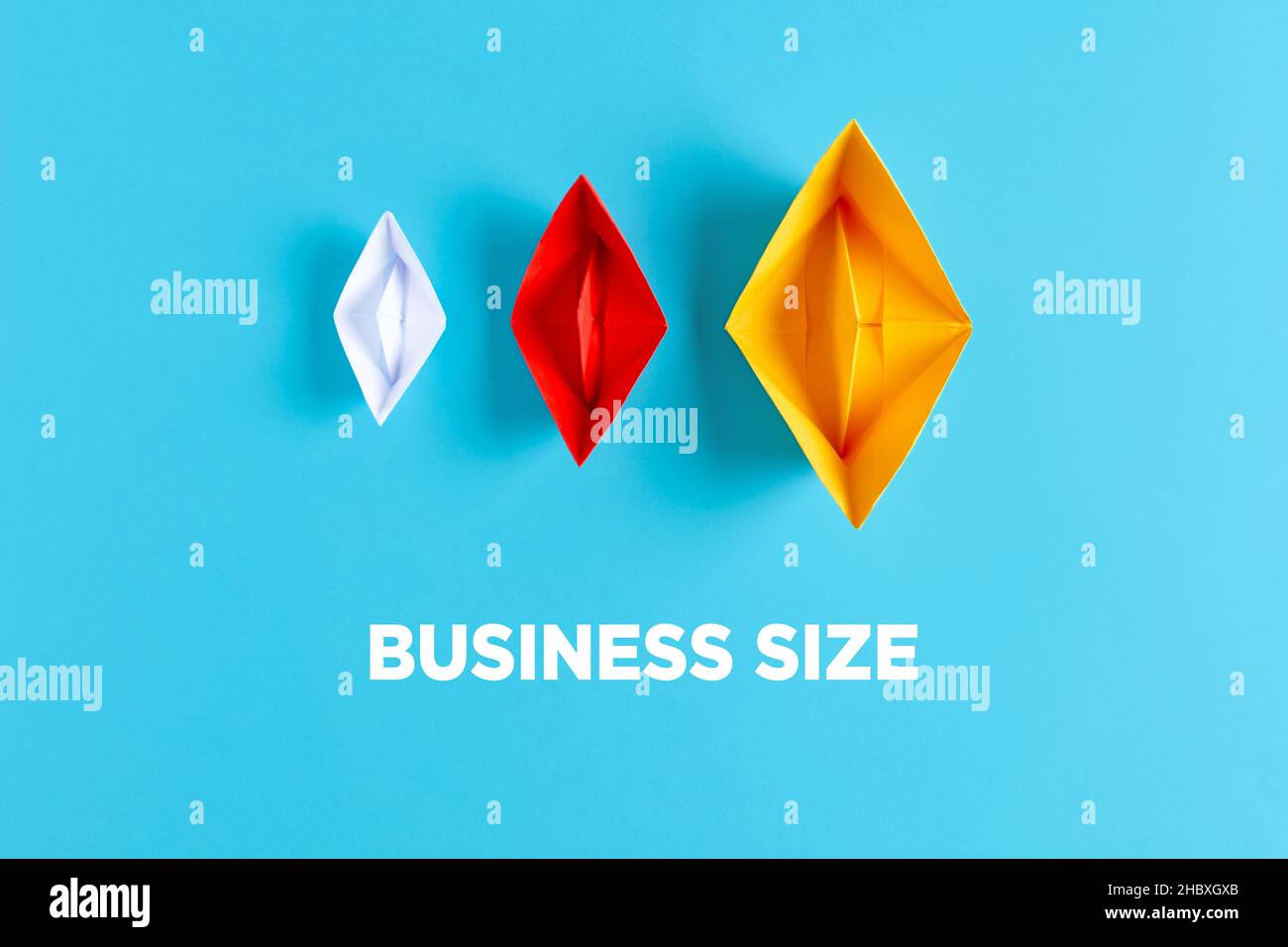 Concepto de tamaño empresarial o empresarial. Tres botes de papel de diferentes tamaños y colores sobre fondo azul con el tamaño del negocio del texto. Foto de stock