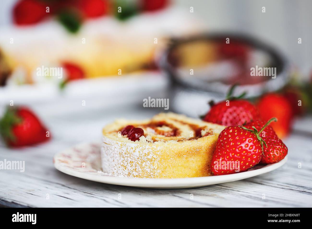 Rollo de pastel de fresas casero o Roulade con relleno de mermelada de bayas y azúcar en polvo con hojas de menta. Postre sobre una tta de madera rústica blanca Foto de stock