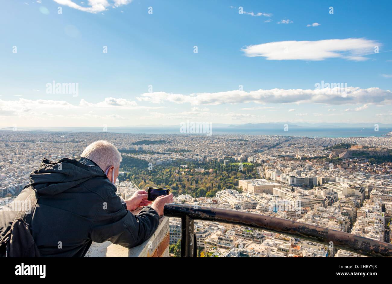 Primer plano horizontal de un turista tomando fotos de la vista de la Acrópolis y la ciudad de Atenas desde el pico más alto de la colina de Lycabettus, Grecia. Foto de stock