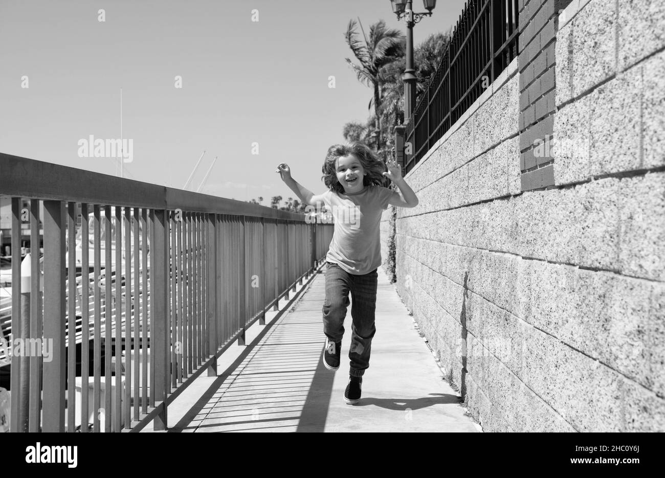 Niño feliz y enérgico disfrute de tiempo libre corriendo en el paseo marítimo durante las vacaciones de verano, libertad Foto de stock