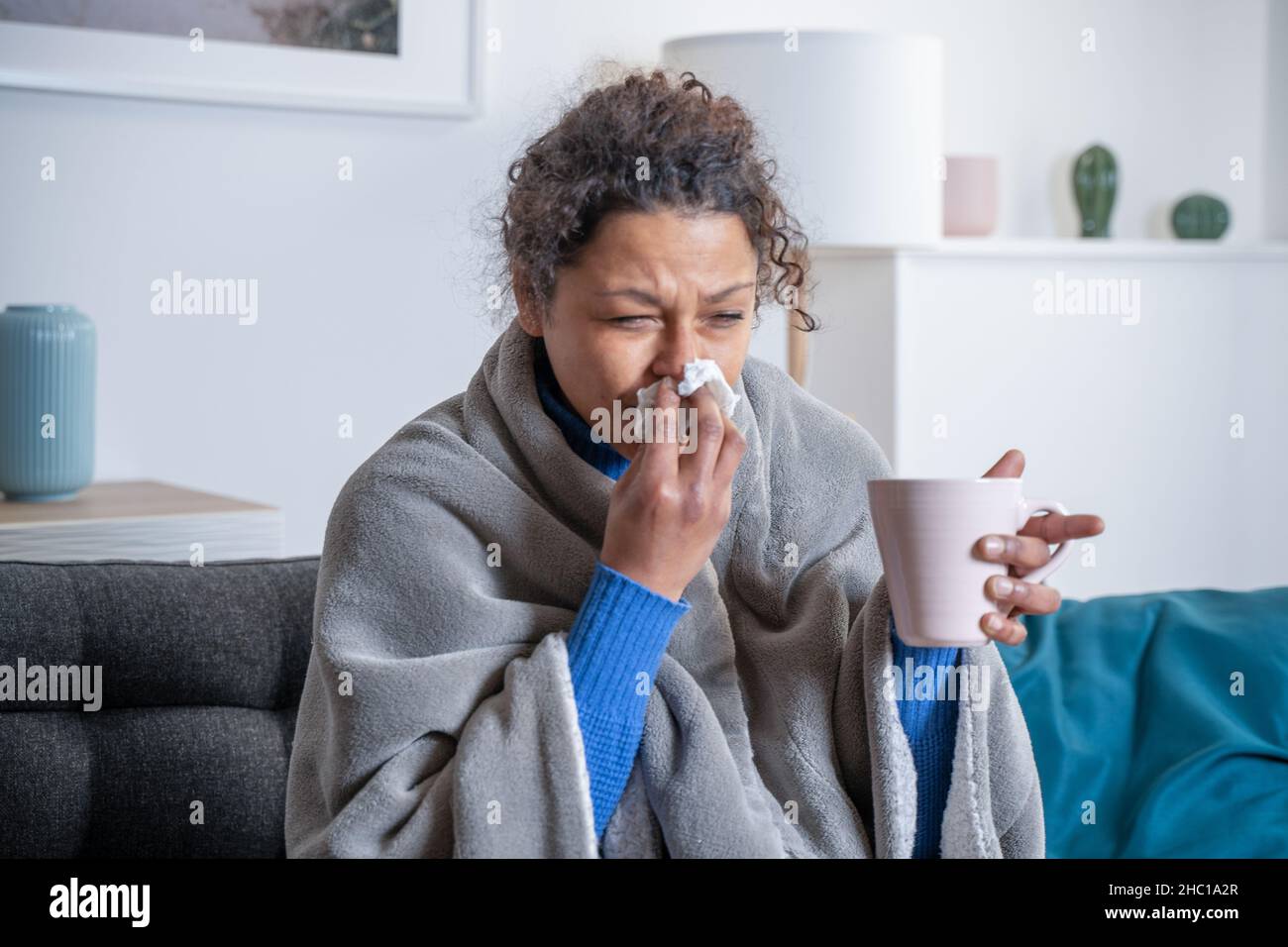 Mujer negra que se siente enferma en casa soplando la nariz Foto de stock