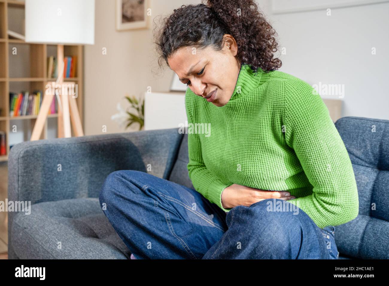 Mujer negra que sufre dolor de estómago en casa en el sofá Foto de stock