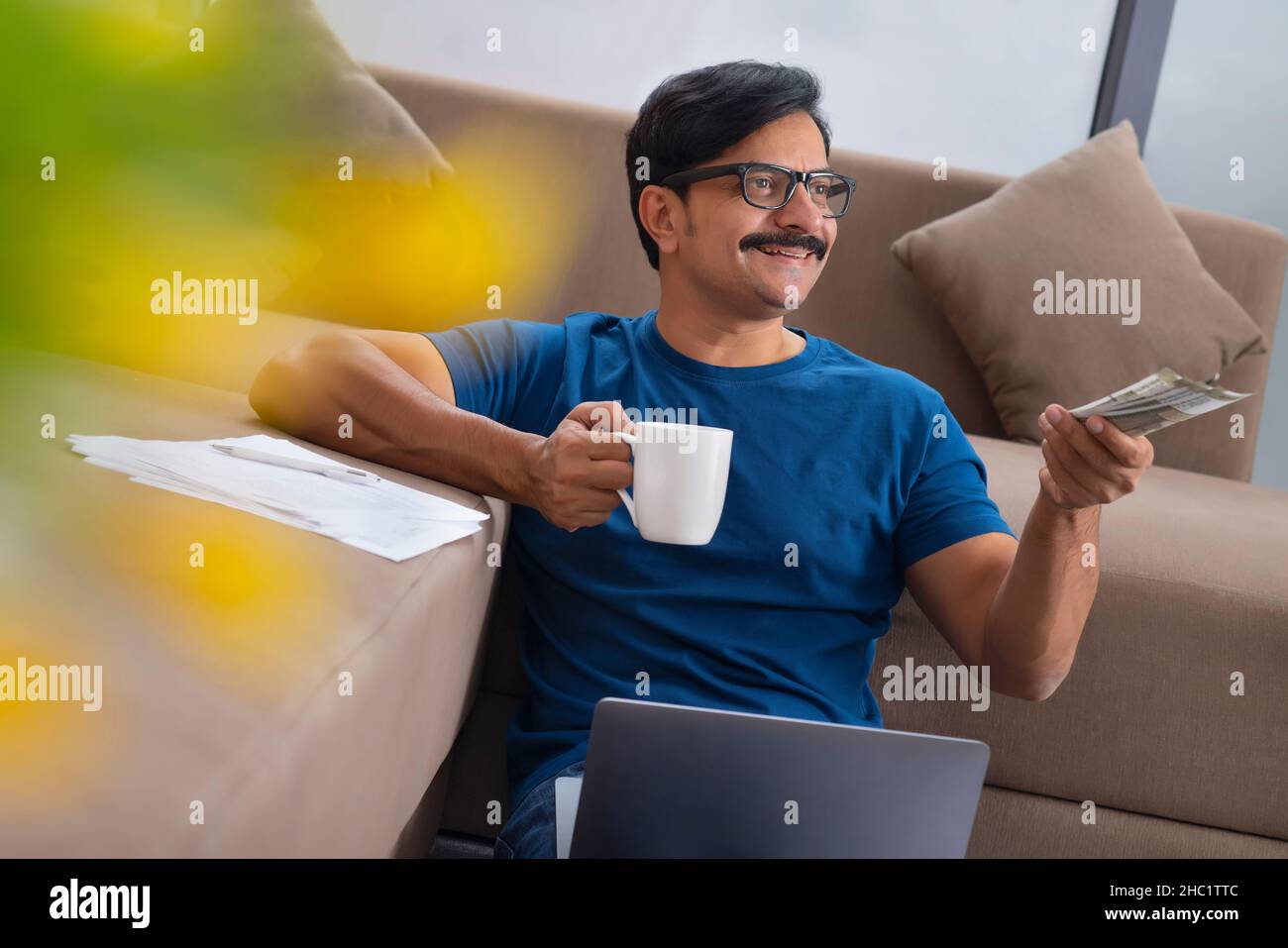 Hombre dando dinero con una taza y un ordenador portátil en su regazo Foto de stock