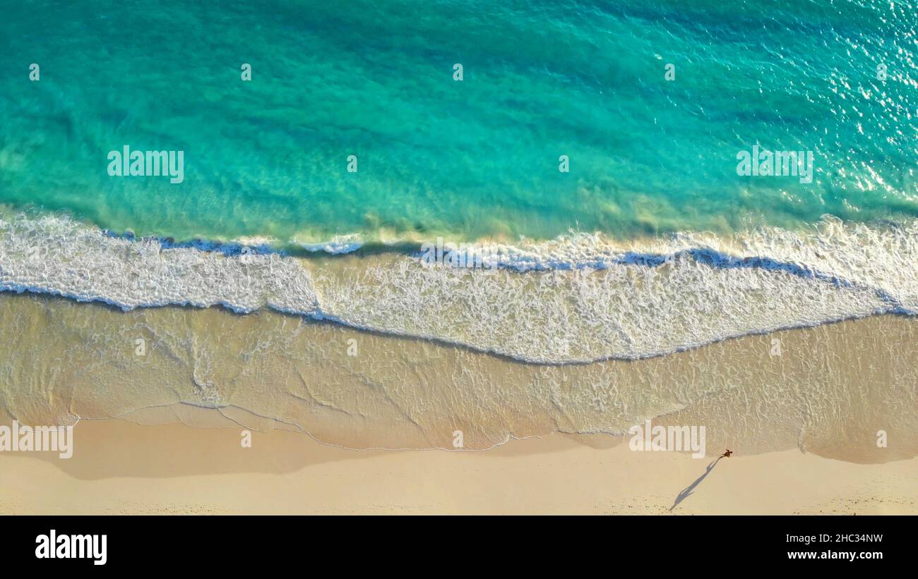 Hombre corriendo a lo largo de la costa del océano, vista de arriba. Vista aérea del hombre a lo largo de la playa de arena blanca a lo largo del increíble océano azul claro. Corre a lo largo de la costa del océano al amanecer. Estilo de vida saludable. Foto de stock