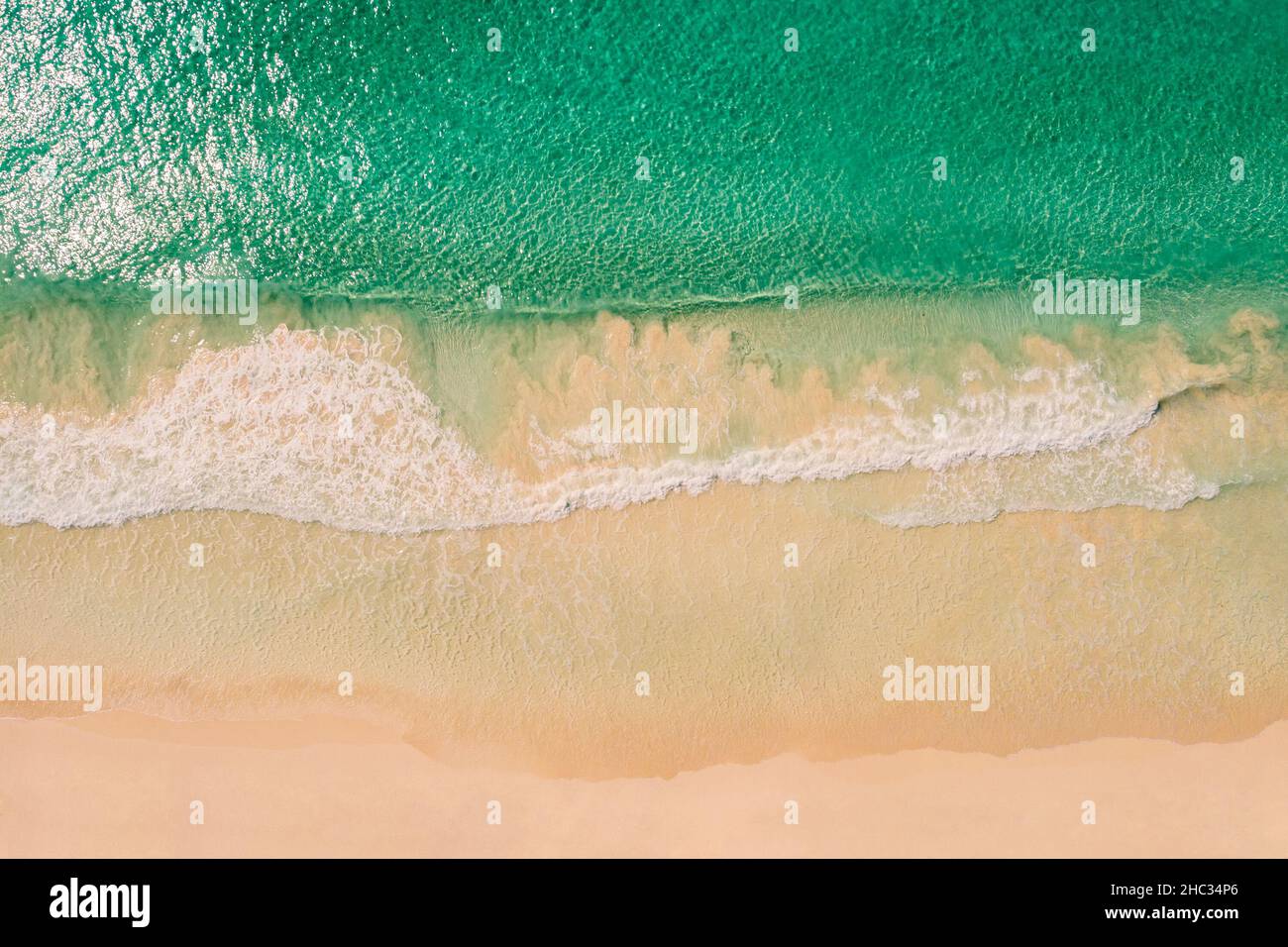 Vista aérea superior de un mar azul transparente con hermosas olas en el día soleado en verano. Paisaje tropical desde el aire del océano con agua azul, fondo arenoso al atardecer. Vista aérea de la playa de arena. Foto de stock