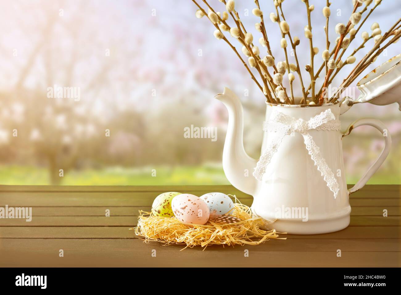 Huevos de Pascua en colores suaves en un nido con el coño willow ramitas una jarra blanca, contra un fondo de jardín de primavera, espacio de copia para el texto Feliz Pascua. Foto de stock