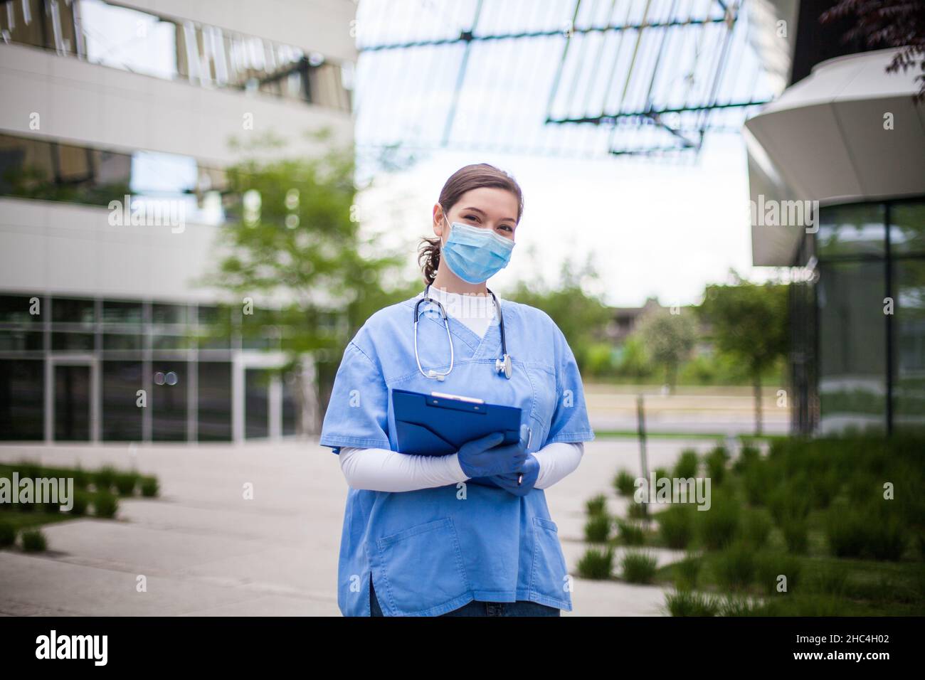 Joven jefa de personal médico con uniforme azul, retrato de especialista clave de primera línea de trabajadores frente a la clínica de la institución de salud o de la clínica de enfermería Foto de stock