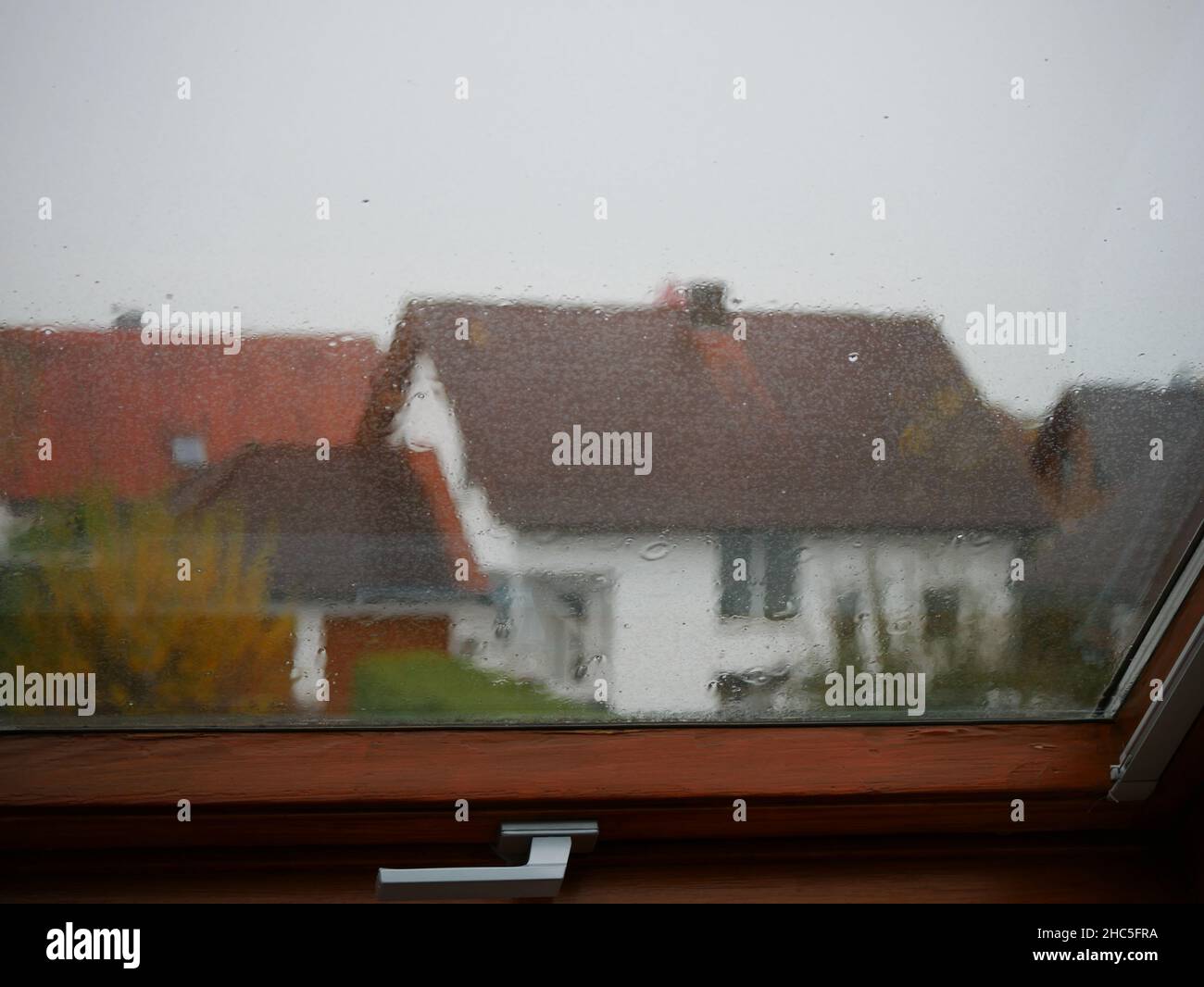 Primer plano de cristal de ventana con gotas de lluvia, casas residenciales desenfocadas en el fondo Foto de stock