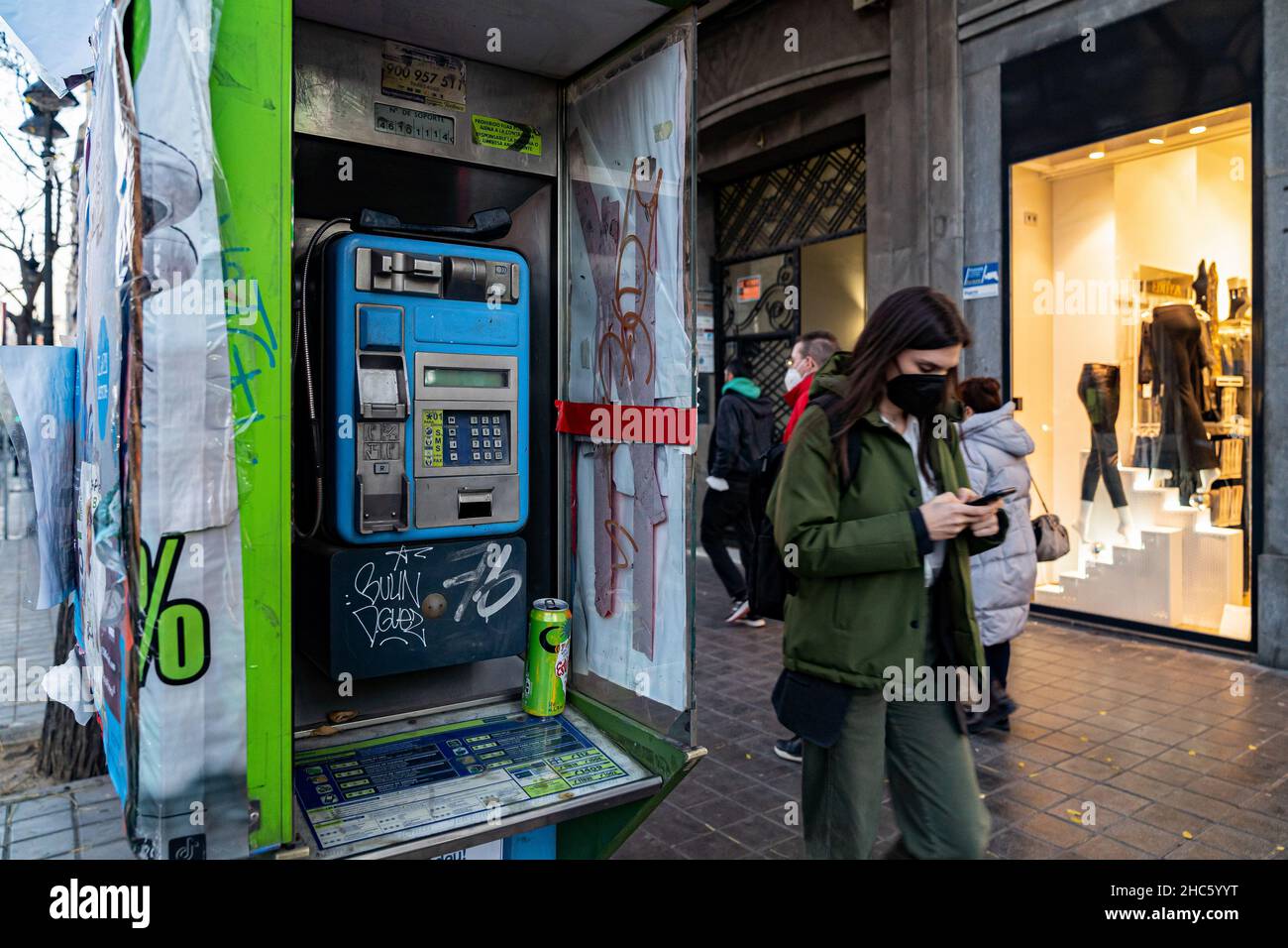 Valencia, España. 15th de Dic de 2021. Una mujer con una máscara hablando en un teléfono móvil pasa delante de una cabina telefónica en Valencia. Según la nueva Ley General de Telecomunicaciones (LGT), las cabinas telefónicas desaparecerán en 2022. La aparición del teléfono móvil ha sido la causa principal de la desutilización de estas cabinas. (Foto de Xisco Navarro/SOPA Images/Sipa USA) Crédito: SIPA USA/Alamy Live News Foto de stock