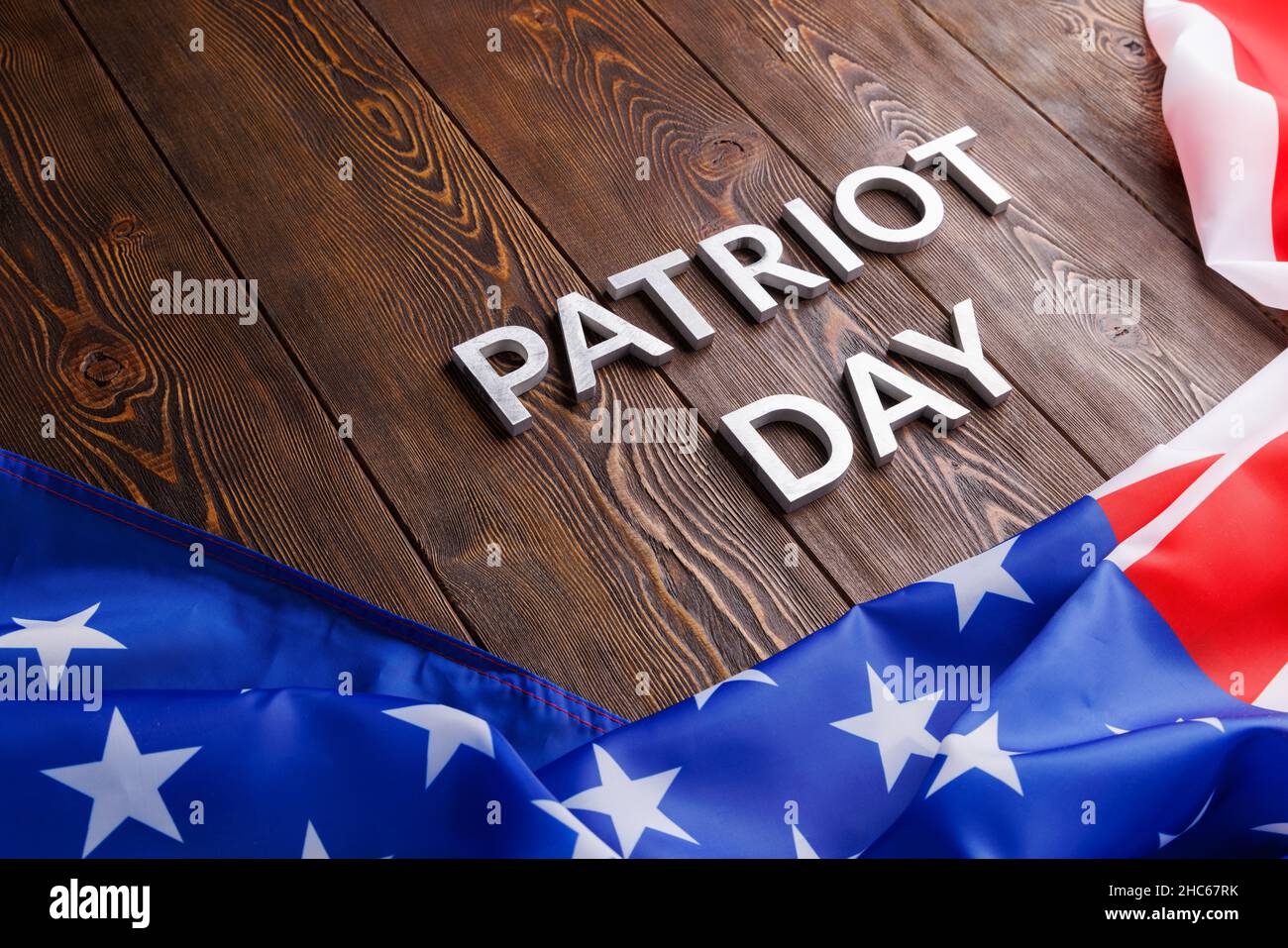 las palabras patriota día puso con letras de metal plateado en la superficie de la tabla de madera con la bandera ee.uu. arrugada Foto de stock