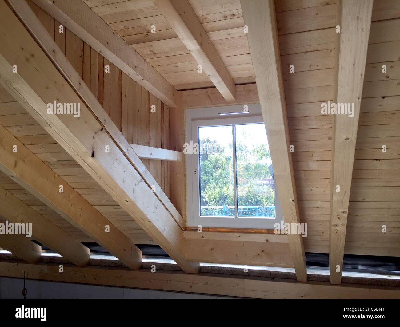 Estructura de madera construcción de un armazón de techo con ventanal en el ático de un nuevo edificio residencial, trabajos de construcción antes del interior c Foto de stock
