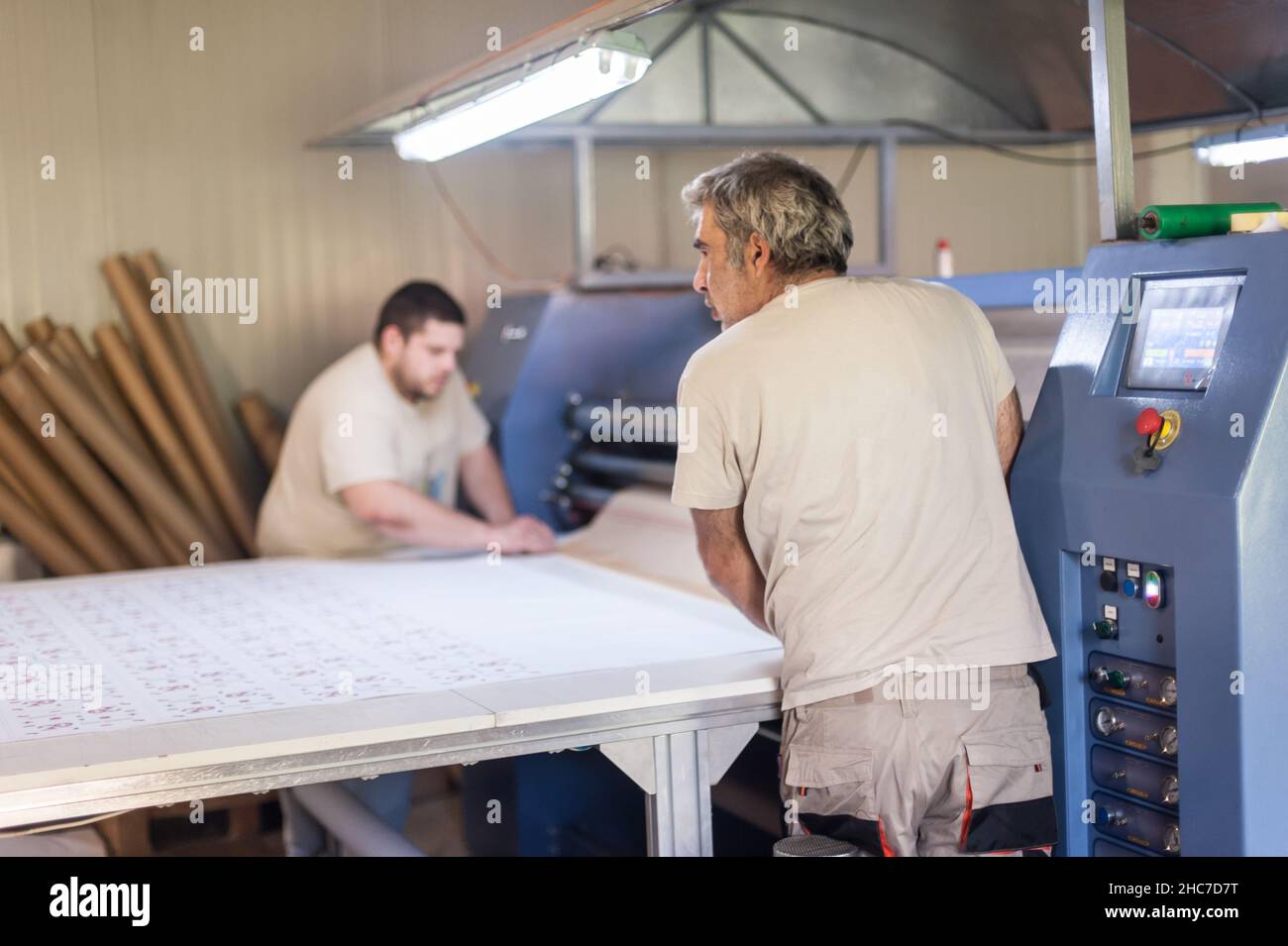 Dos técnicos trabajadores operador trabaja en tela de primera calidad industrial de sublimación rodillo de impresión por calor en la imprenta digital o Foto de stock