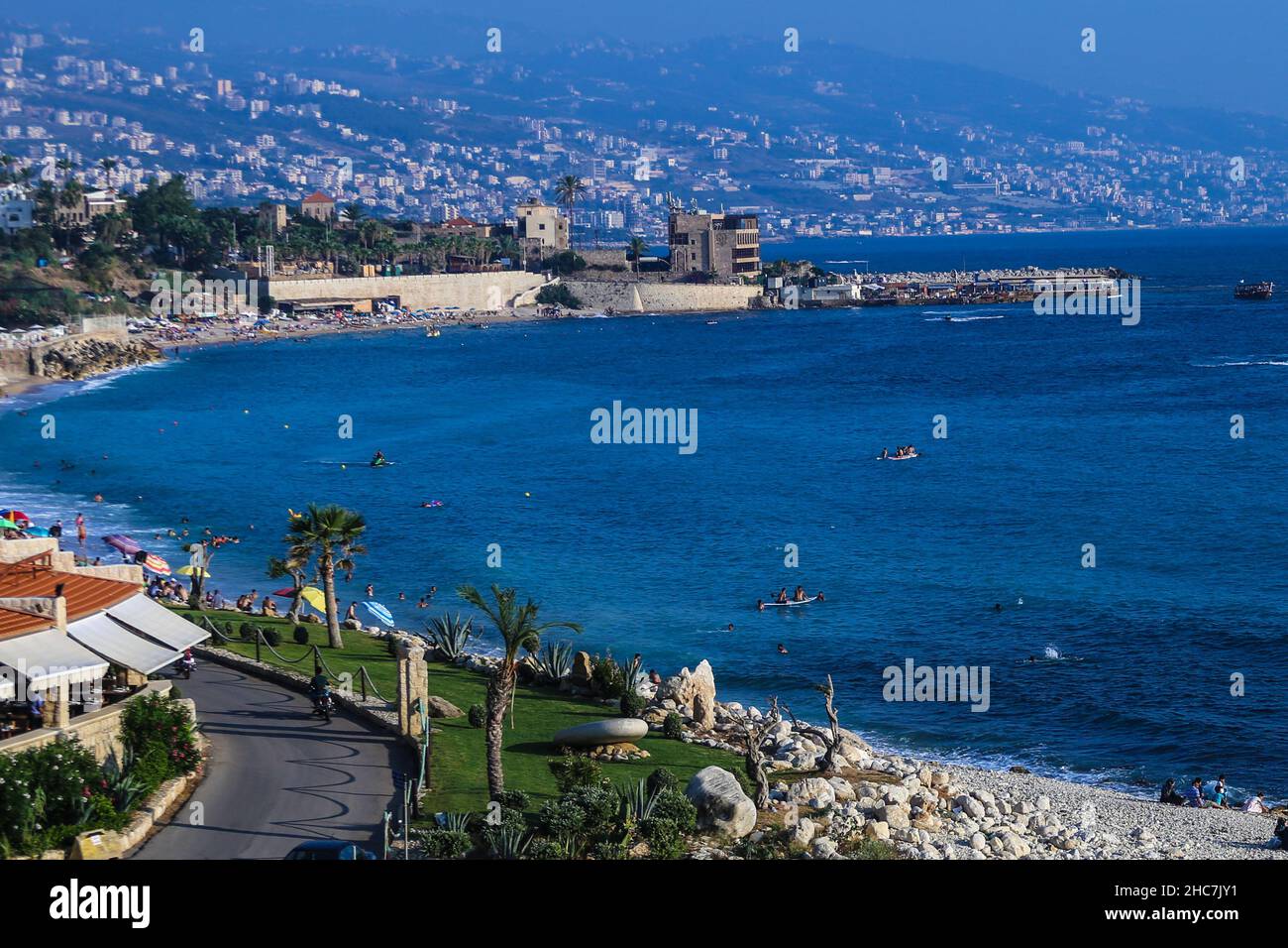 Vista panorámica de un paisaje marino desde el casco antiguo de la ciudad de Byblos con palmeras y construcciones en la ladera de la montaña Foto de stock