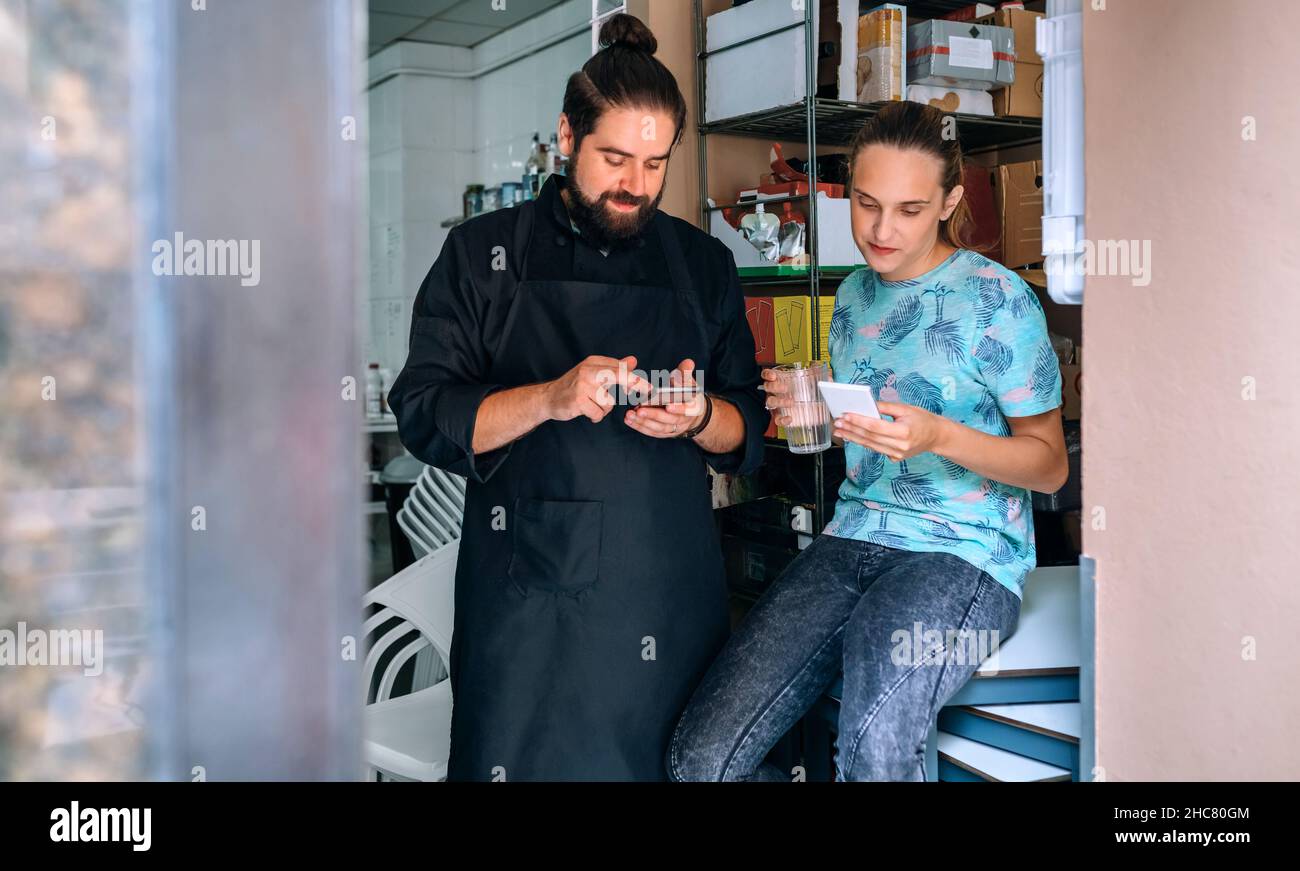 Cocinera y camarera mirando móvil durante la pausa Foto de stock