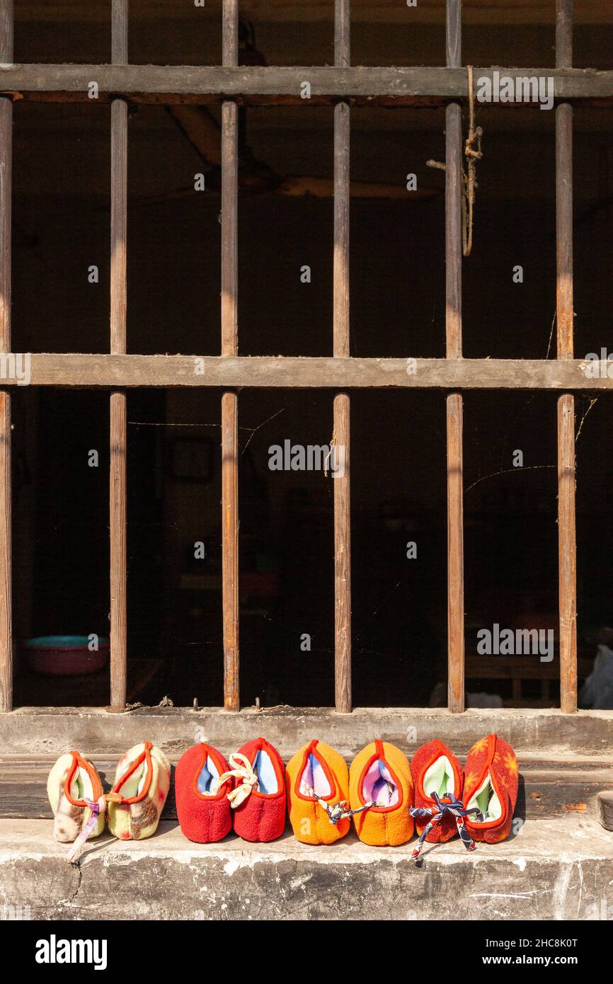 Coloridas zapatillas secando al sol frente a una ventana con barras de hierro. Xitang, China Foto de stock