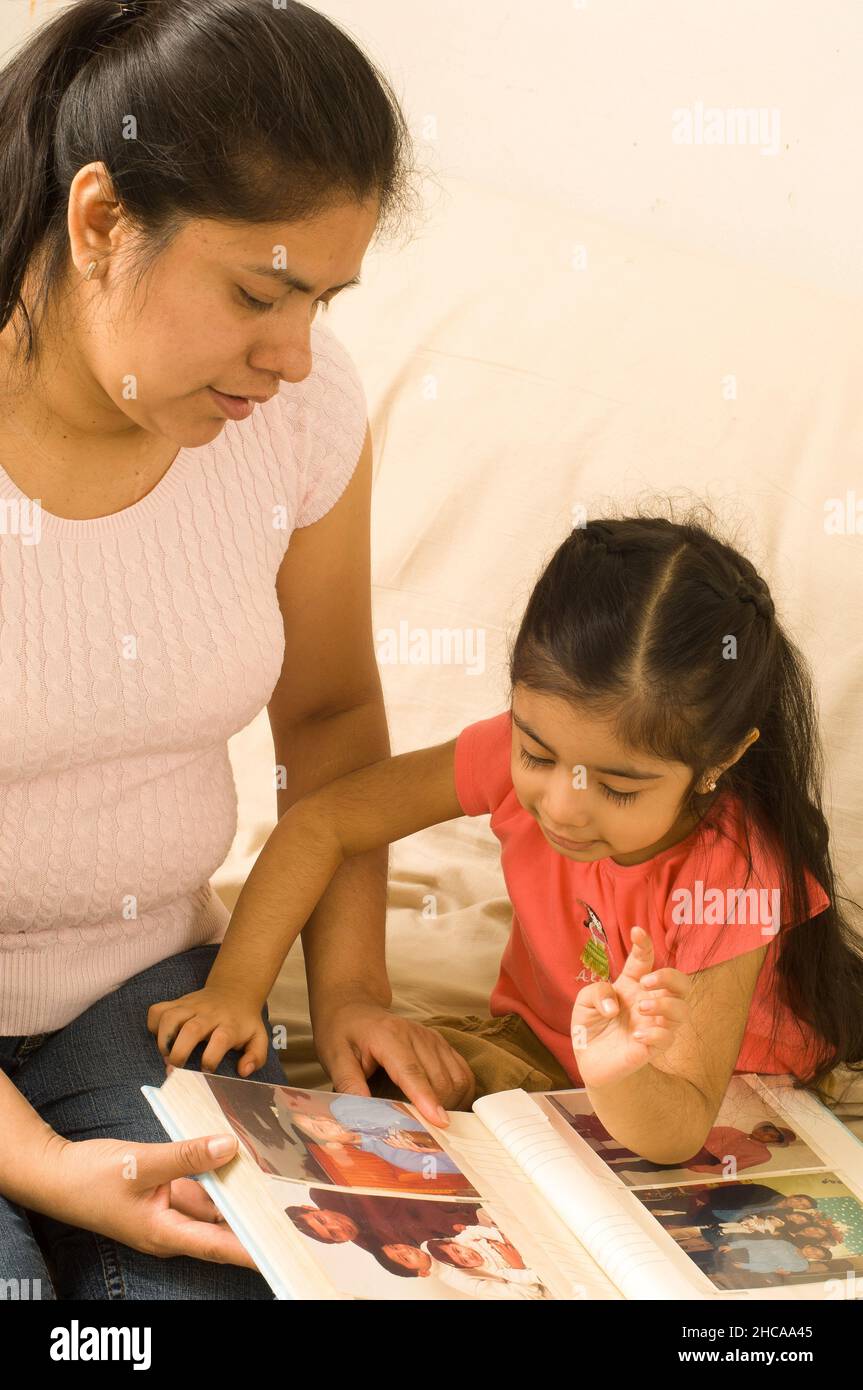 niña de 3 años en casa con madre mirando fotografías familiares en el álbum hablando e interactuando Foto de stock