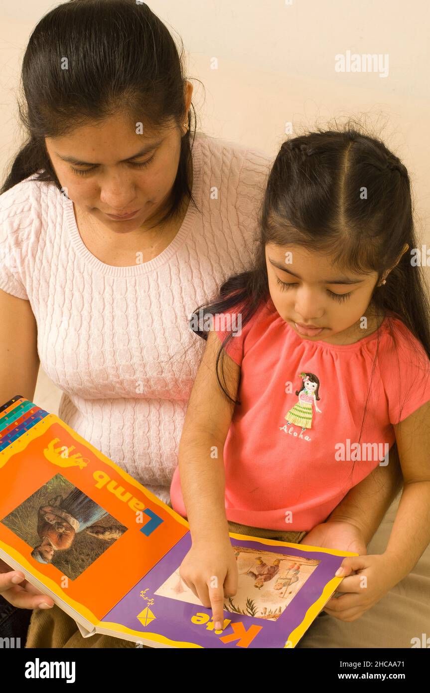 niña de 3 años en casa con madre interacción leyendo libro y hablando niño apuntando a la ilustración Foto de stock