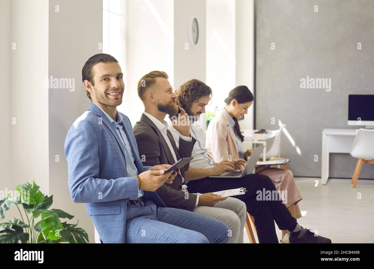 Feliz hombre utilizando un tablet mientras espera en línea con otras personas de negocios Foto de stock