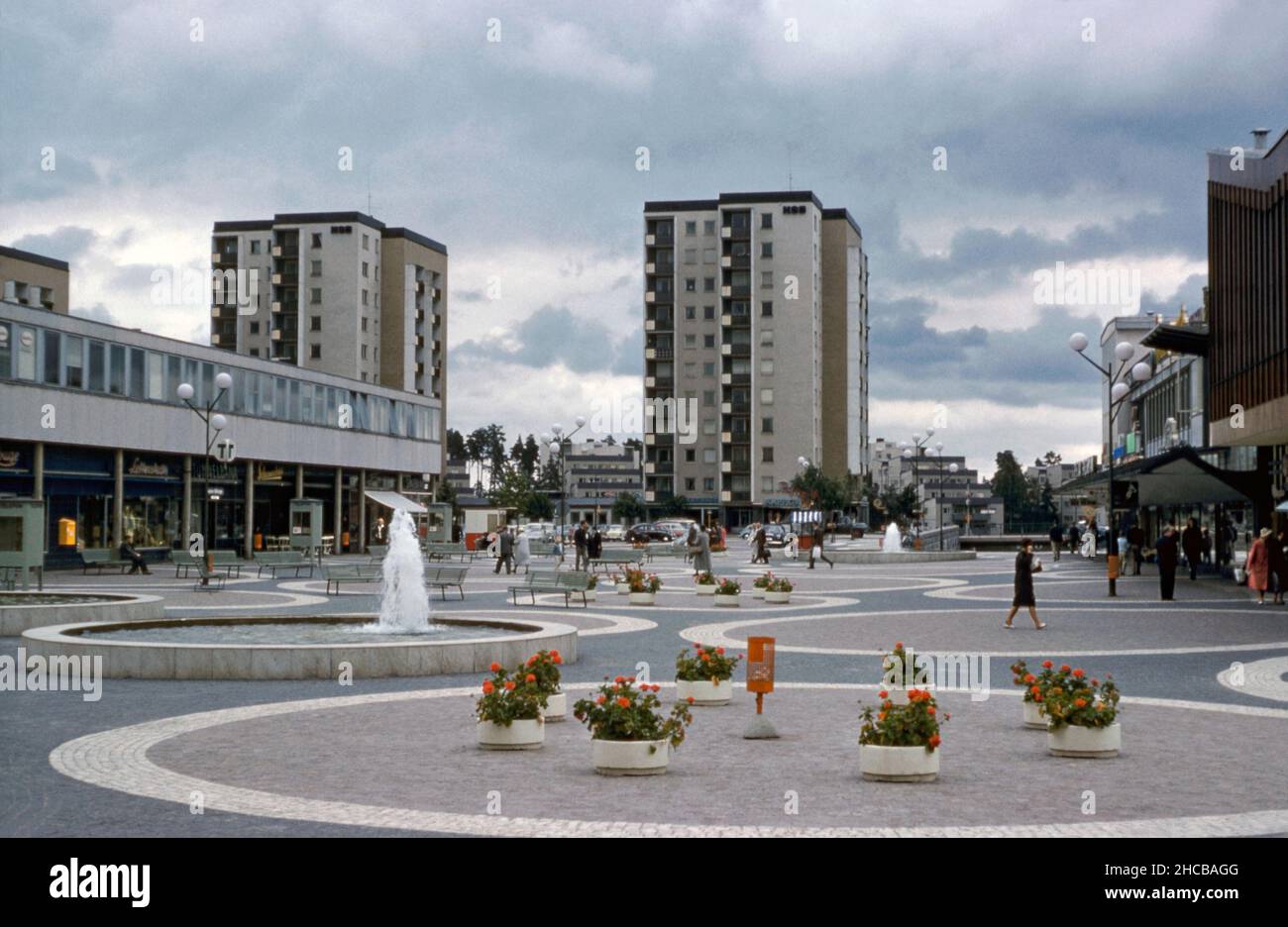 Una vista de 1961 del Vällingby Centrum, el centro comercial del moderno suburbio de posguerra de Vällingby en el noroeste de Estocolmo, Suecia. La plaza central alberga a menudo un mercado. El metro de Estocolmo pasa por el centro. La señal 'T' (izquierda) indica una entrada a la estación debajo de la plaza. Esta imagen es de una transparencia de color de 35mm Agfacolor amateur, una fotografía de 1960s. Foto de stock