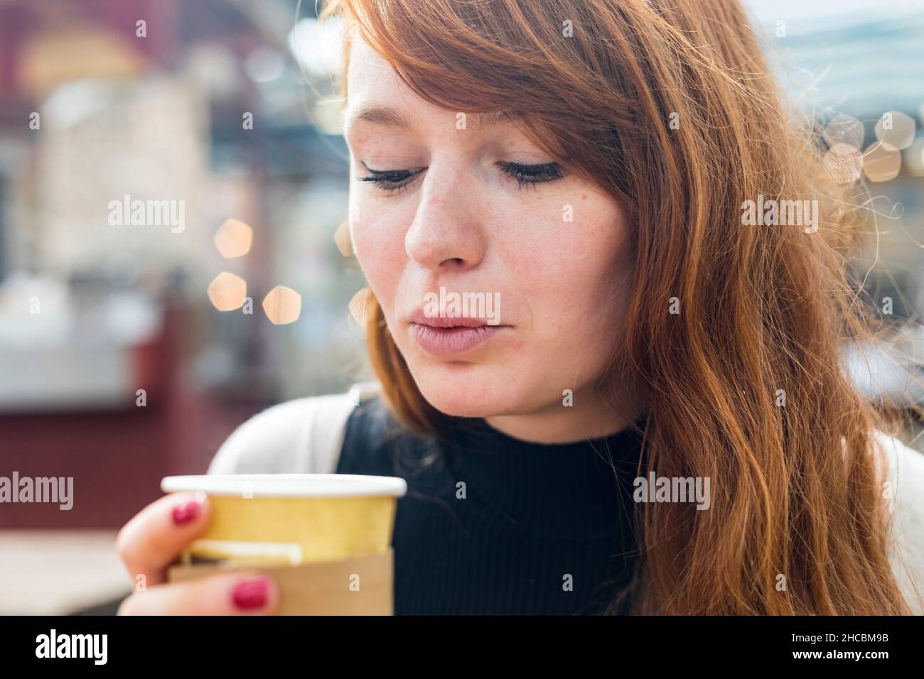 Mujer soplando café en una taza desechable en el café Foto de stock