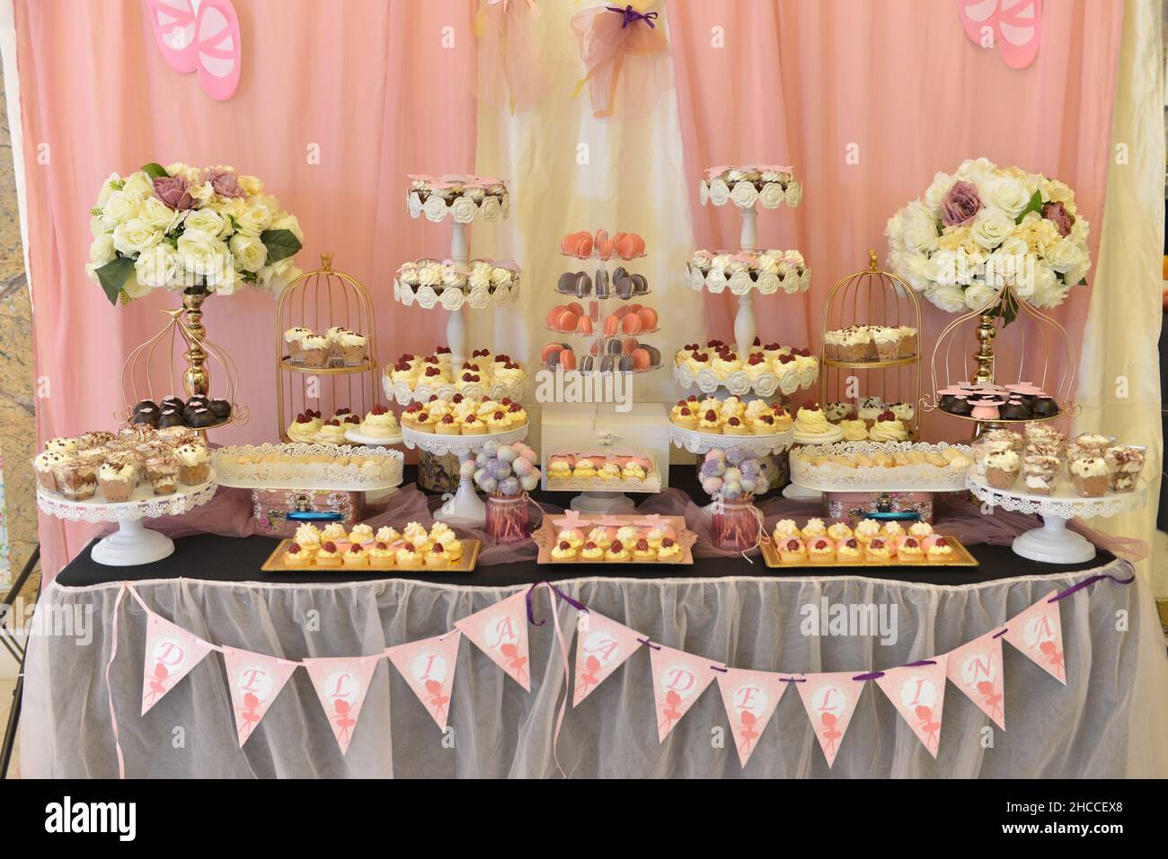Mesa de banquetes de pasteles bellamente decorados con ramos de flores en un mantel listo para un evento Foto de stock