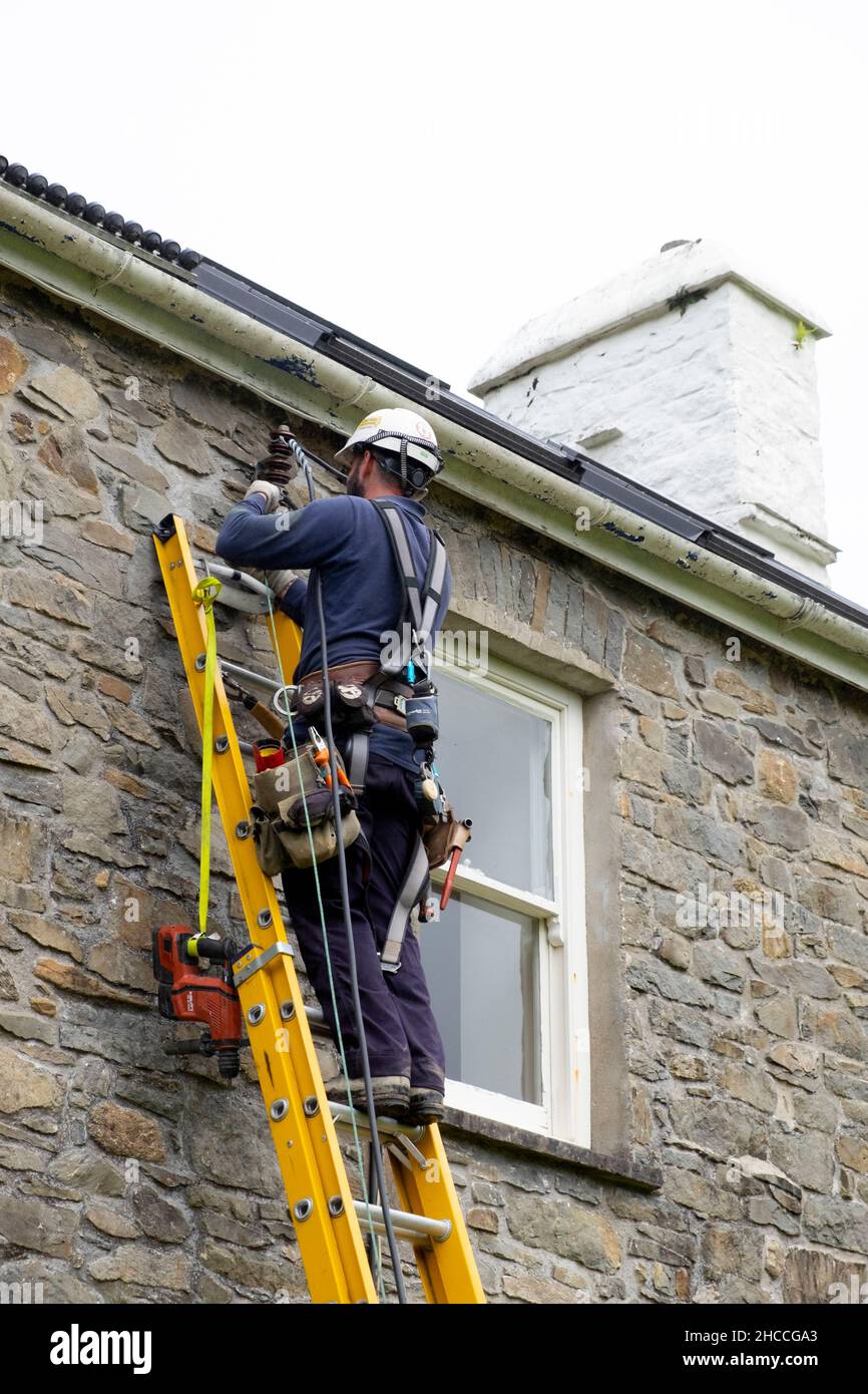 Trabajador de electricidad que trabaja conectando cables de equipo de suministro eléctrico en casa de piedra de propiedad rural en Gales Reino Unido Gran Bretaña 2021 KATHY DEWITT Foto de stock