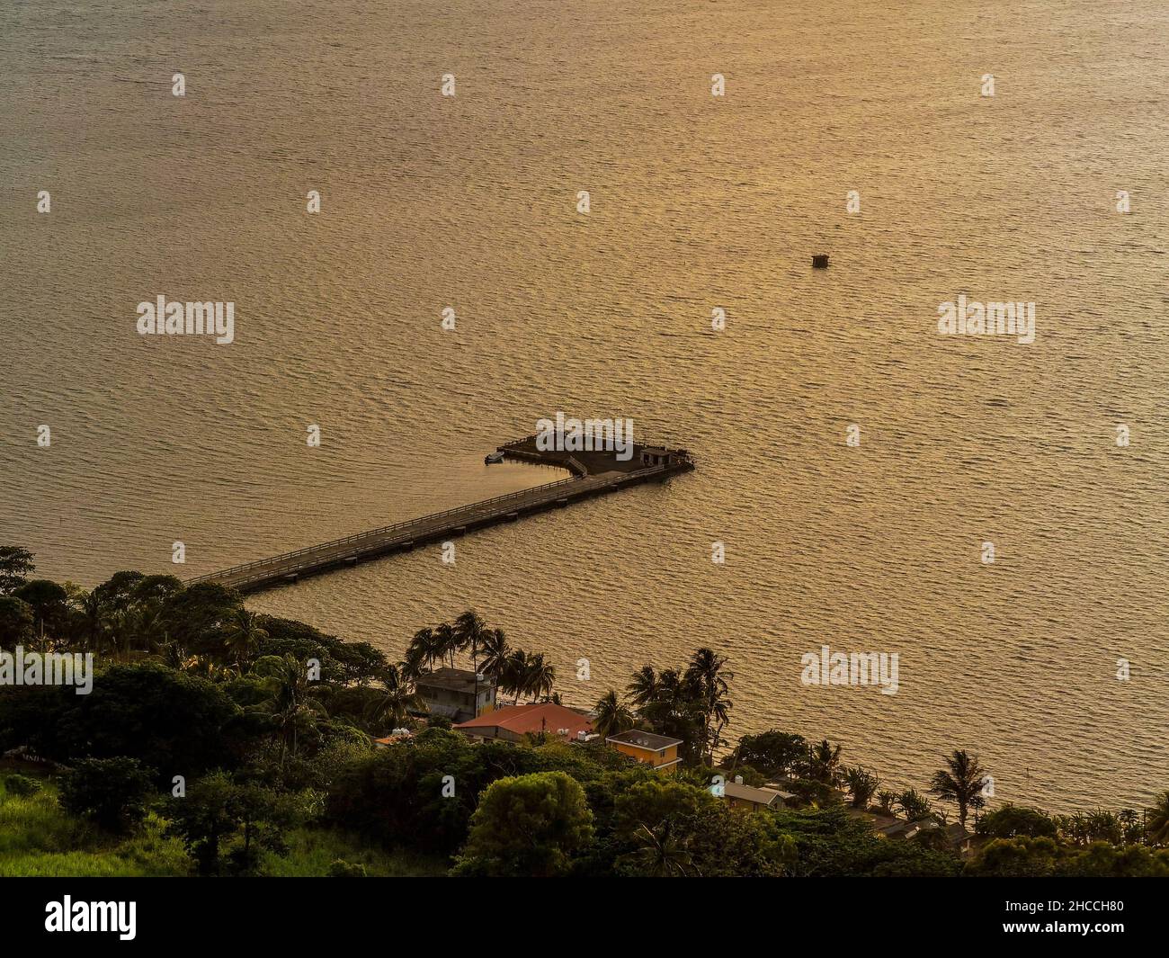 Vista fascinante de la tierra verde con un muelle sobre las tranquilas aguas del mar al atardecer Foto de stock
