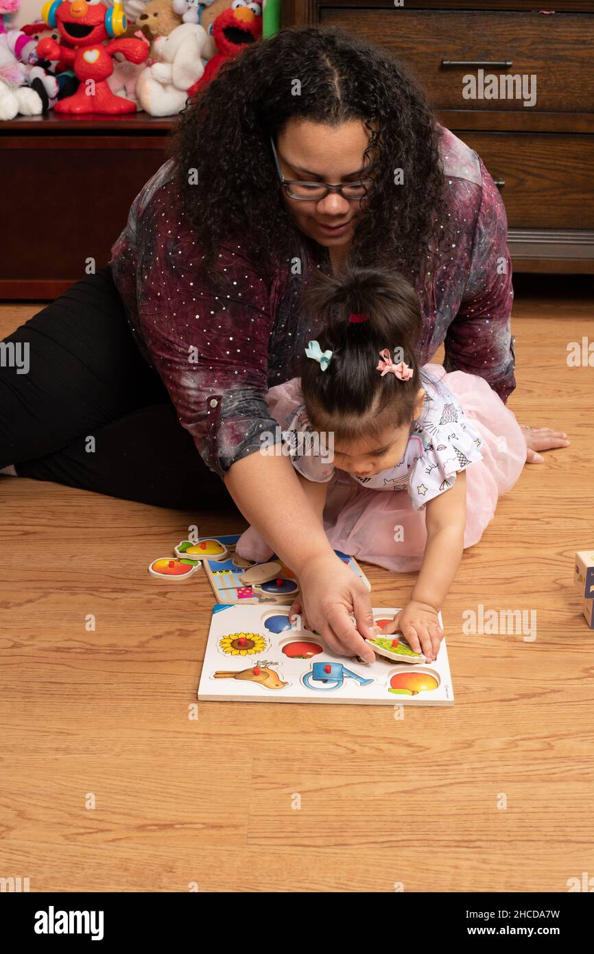 niña de 17 meses con madre jugando con la pieza de puzzle de la clavija madre ayudándola Foto de stock