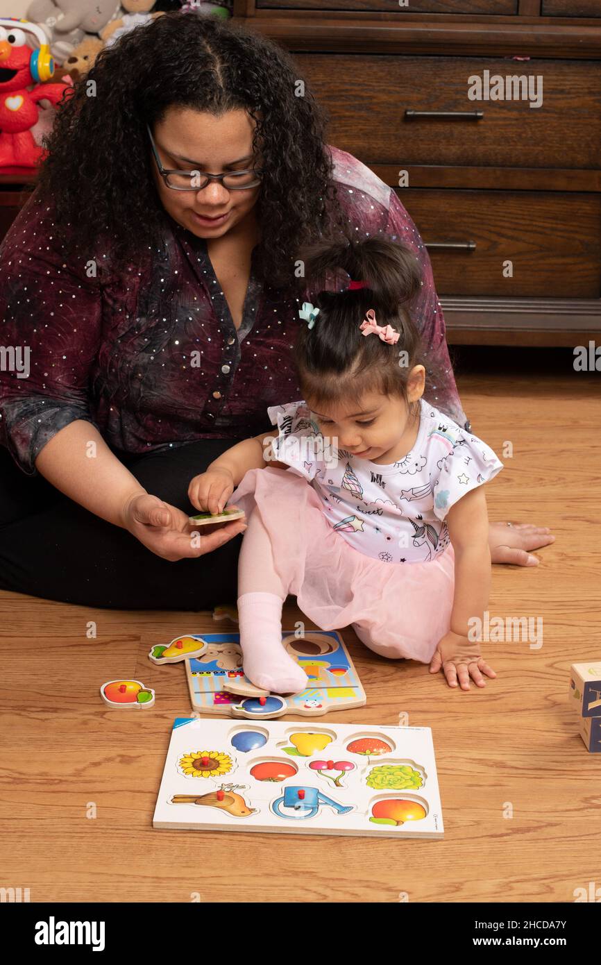 niña de 17 meses con madre jugando con la pieza de puzzle de la clavija madre ayudándola, hablando con ella Foto de stock