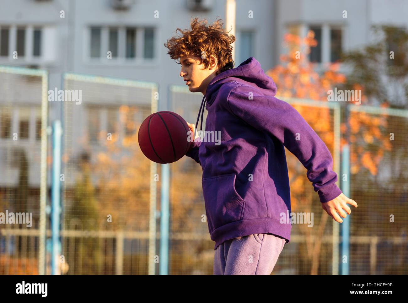 Lindo adolescente con sudadera violeta jugando al baloncesto. Ni o
