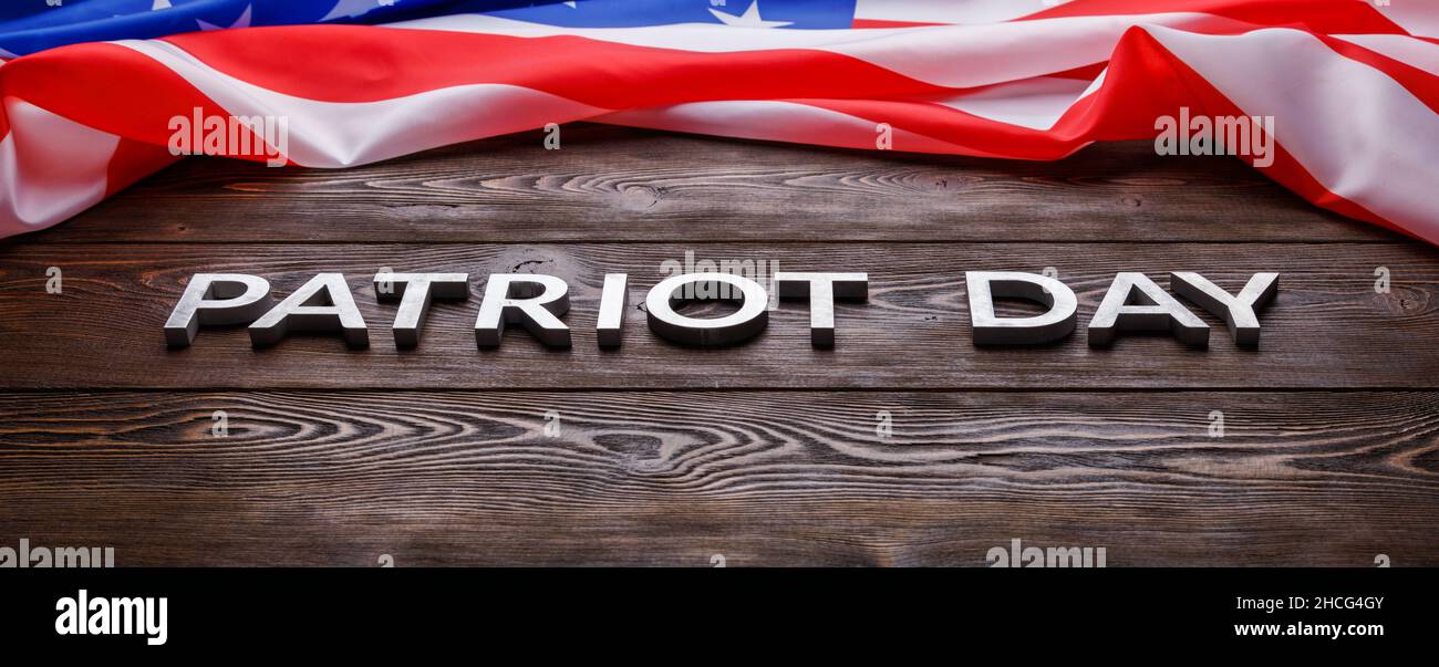 las palabras patriota día puso con letras de metal plateado en la superficie de la tabla de madera con la bandera ee.uu. arrugada Foto de stock