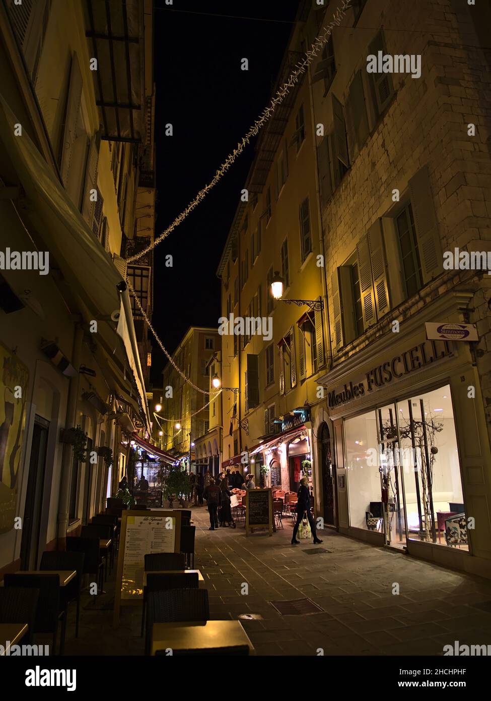 Animada escena nocturna en el centro de Niza, Francia en la Riviera Francesa con gente caminando a través de un callejón iluminado, restaurantes y tiendas. Foto de stock
