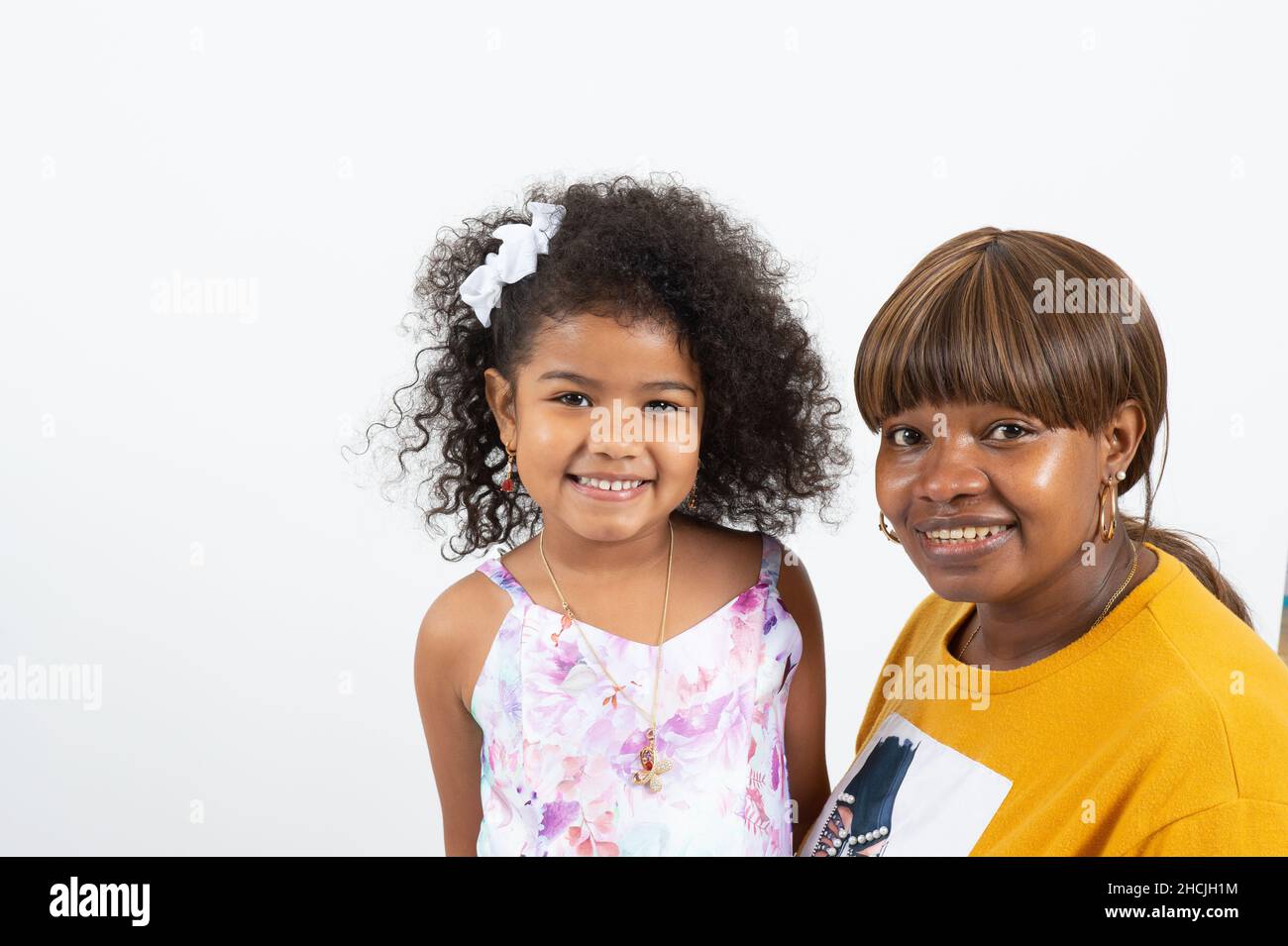 niña de 4 o 5 años con madre sonriendo posando para retrato sobre un fondo blanco Foto de stock