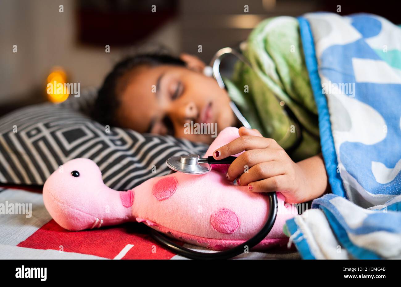 Niño adolescente durmiendo sosteniendo el estetoscopio y la muñeca en la cama - concepto del deseo que se convierte en médico, sueños de la infancia y aspiraciones. Foto de stock