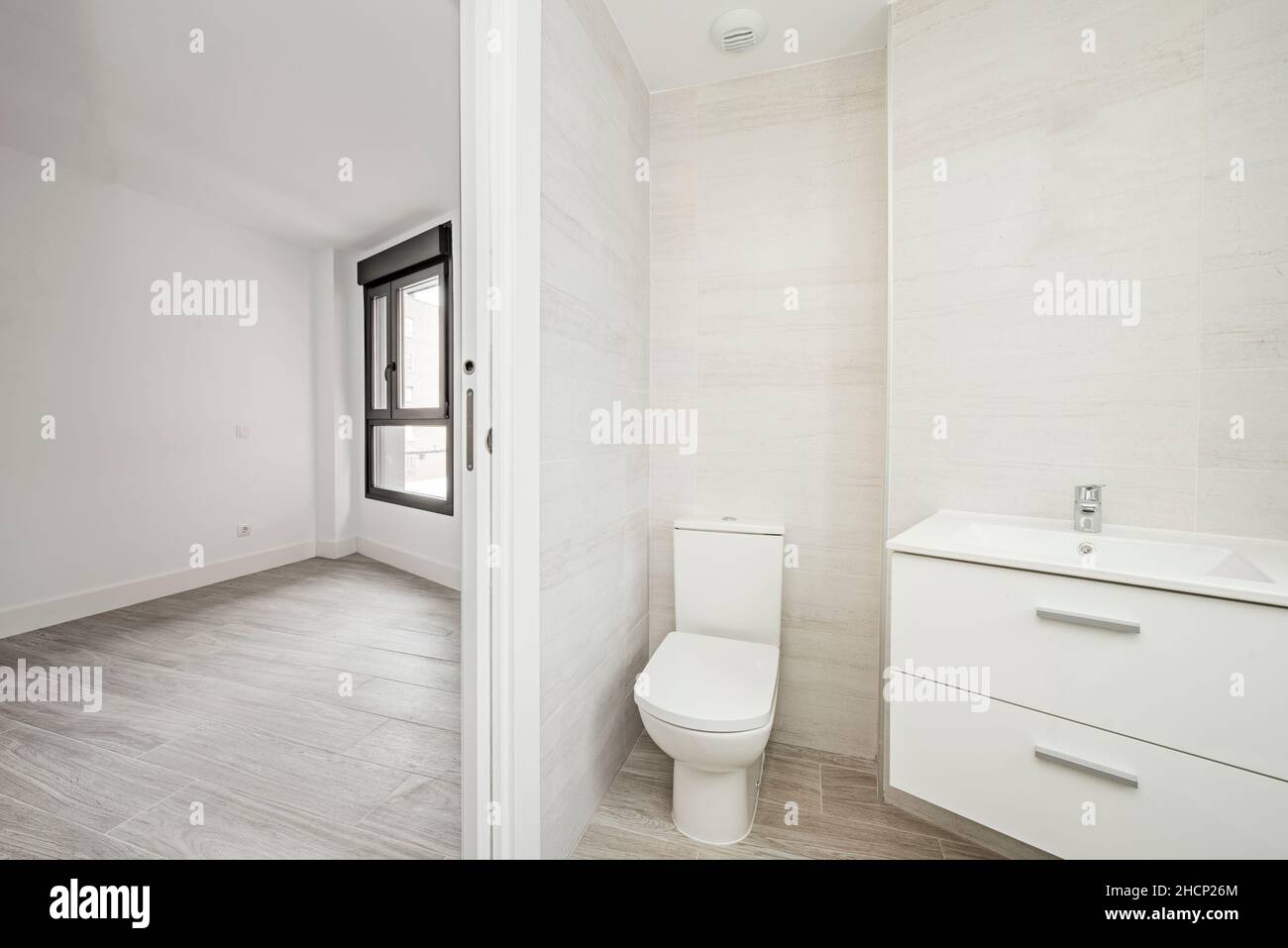 Inodoro con armario y lavabo blanco junto a una habitación vacía Foto de stock