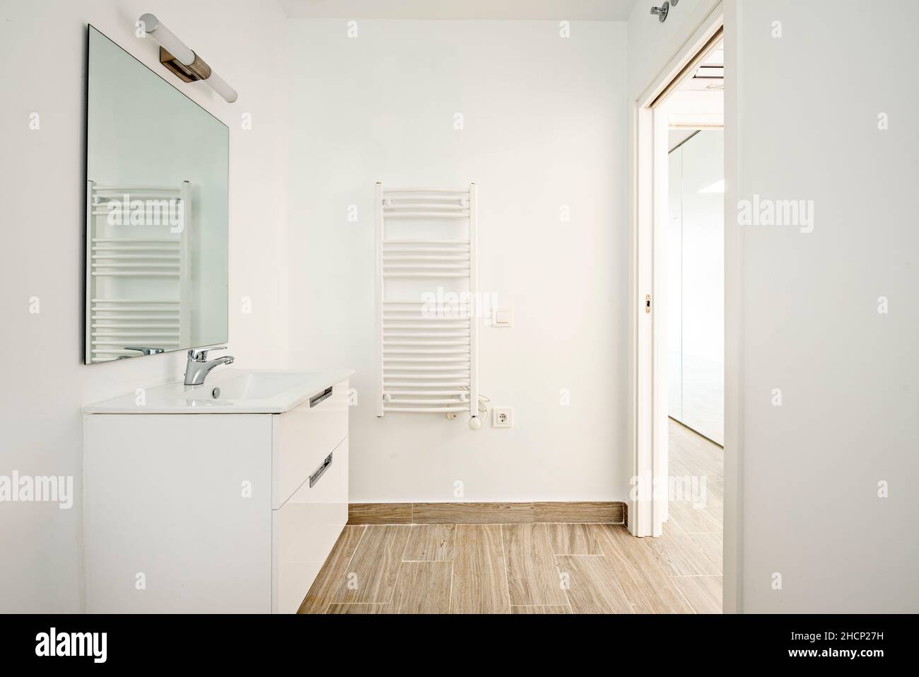 inodoro blanco con suelos de baldosas de madera, radiador montado en la pared y espejo Foto de stock