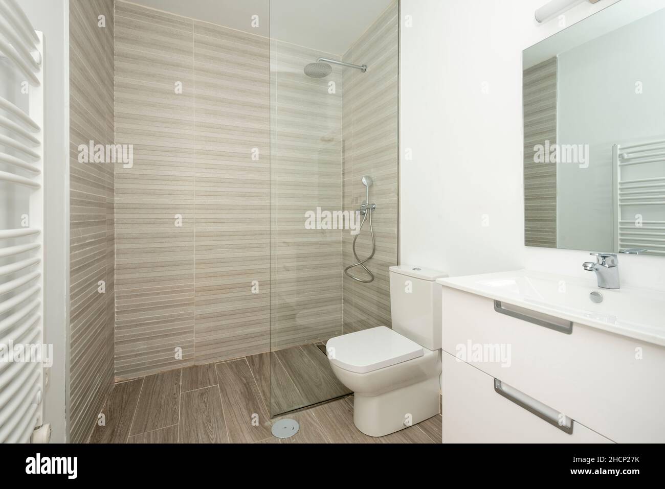 inodoro blanco con pisos de baldosas de madera, espejo de radiador montado en la pared y una amplia ducha con techo de cristal Foto de stock
