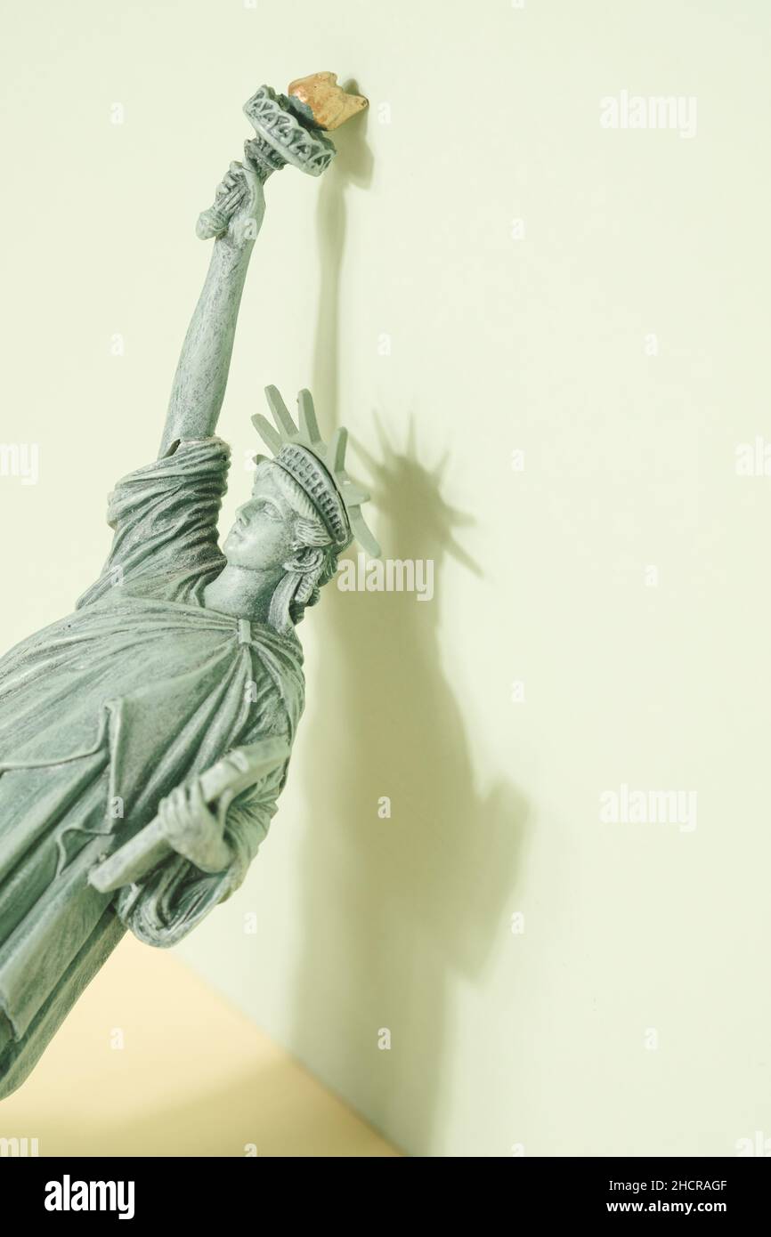 Estatua de la libertad figurita apoyada sobre el fondo verde pastel. Concepto mínimo de la economía ESTADOUNIDENSE. Foto de stock