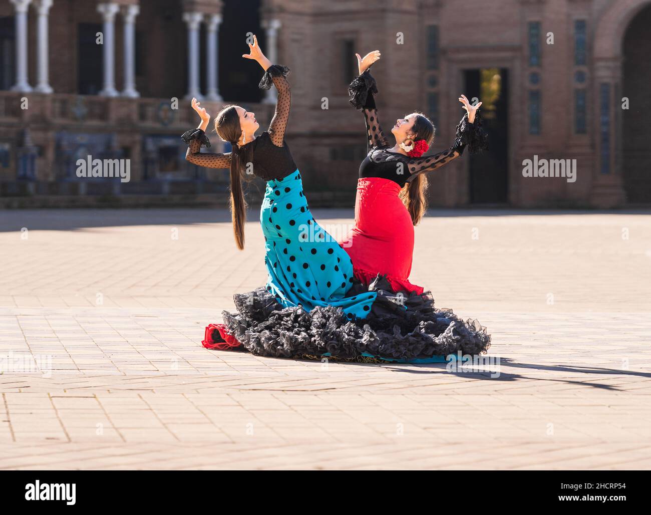 Dos mujeres vestidas con traje flamenco haciendo una coreografía en una plaza Foto de stock