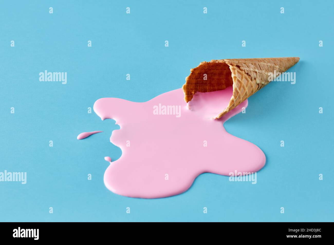 El helado rosa se derrite y derrama del cono de gofre sobre fondo azul pastel. Concepto minimalista de comida de verano. Foto de stock