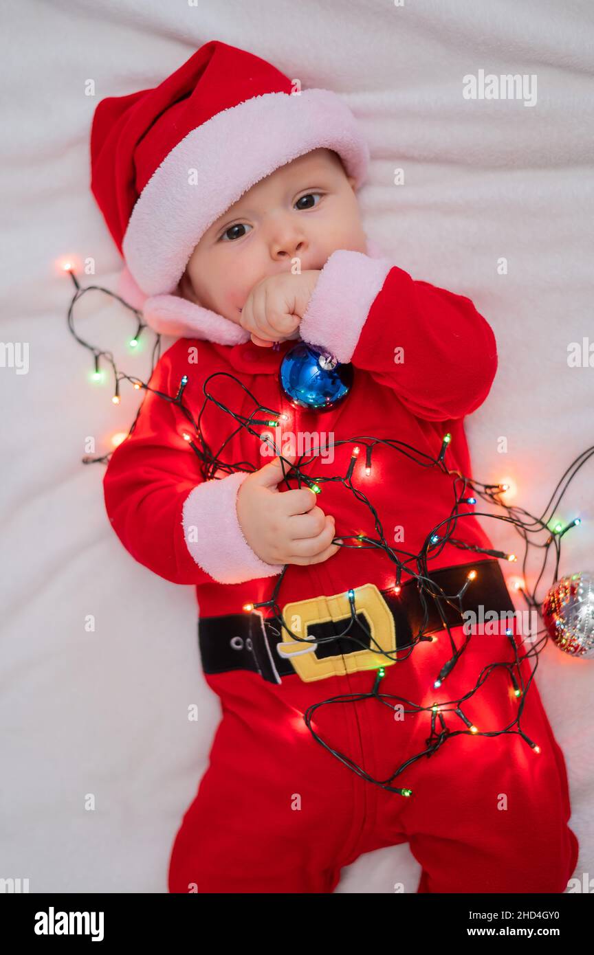 Un niño vestido con un traje de papá noel yace en la cama y juega con un  guirnalda de Navidad Fotografía de stock - Alamy