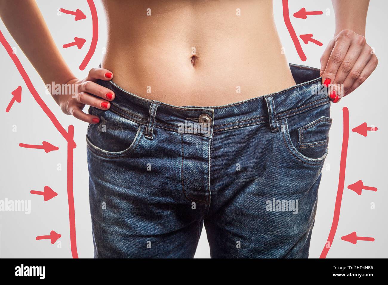 Primer plano de cintura delgada de mujer joven de pie en jeans grandes que muestran una pérdida de peso exitosa, estudio de interior tiro, aislado sobre fondo gris claro, concepto de dieta. Foto de stock