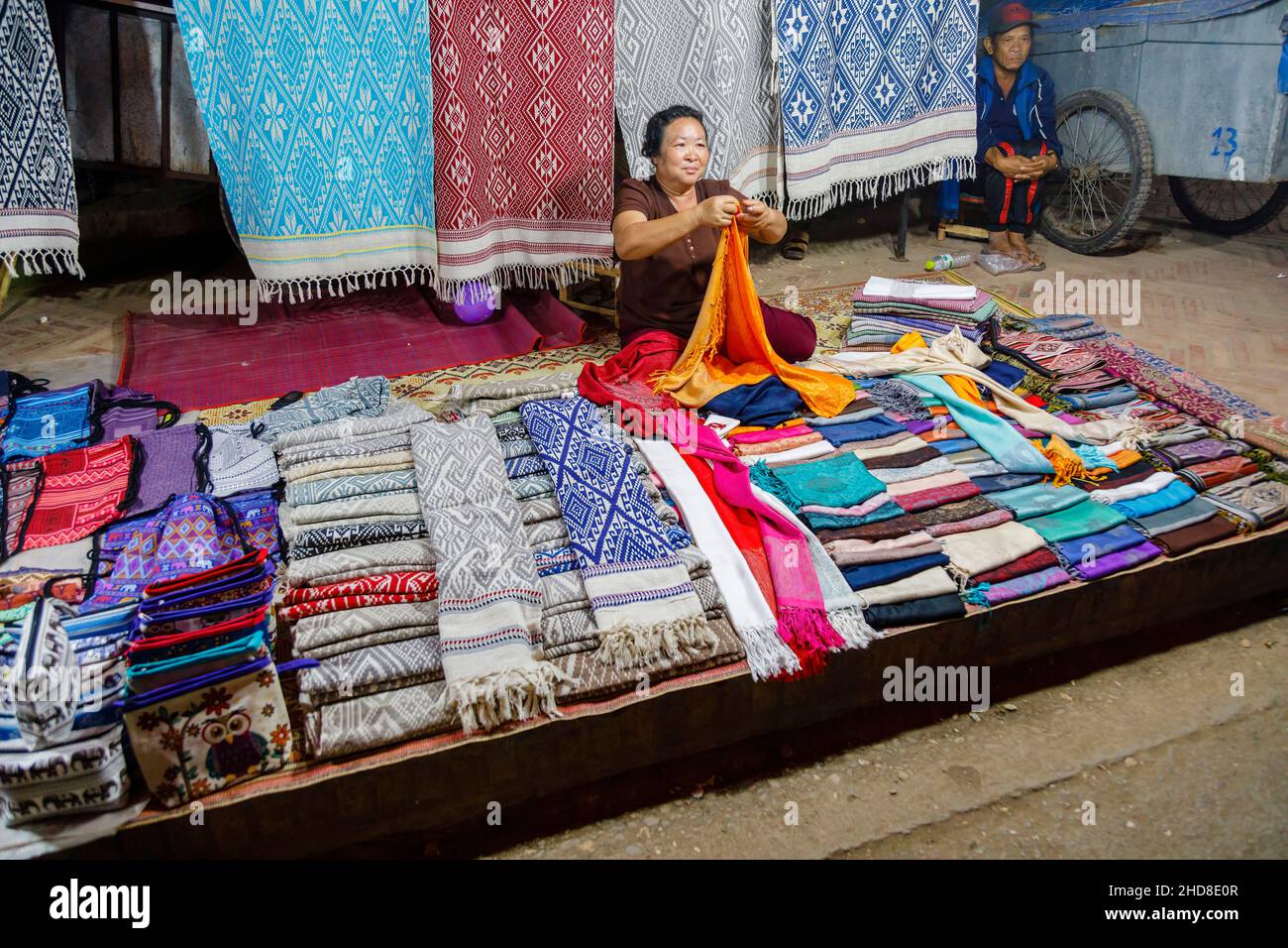 Estallholder femenino local que vende telas en el mercado nocturno de la calle peatonal en el centro de Luang Prabang, norte de Laos, sudeste de Asia Foto de stock
