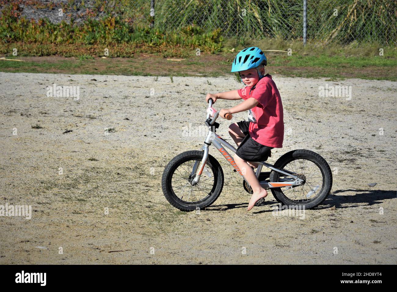 Niño montando su bicicleta con un casco en la arena de Morro Bay CA Foto de stock