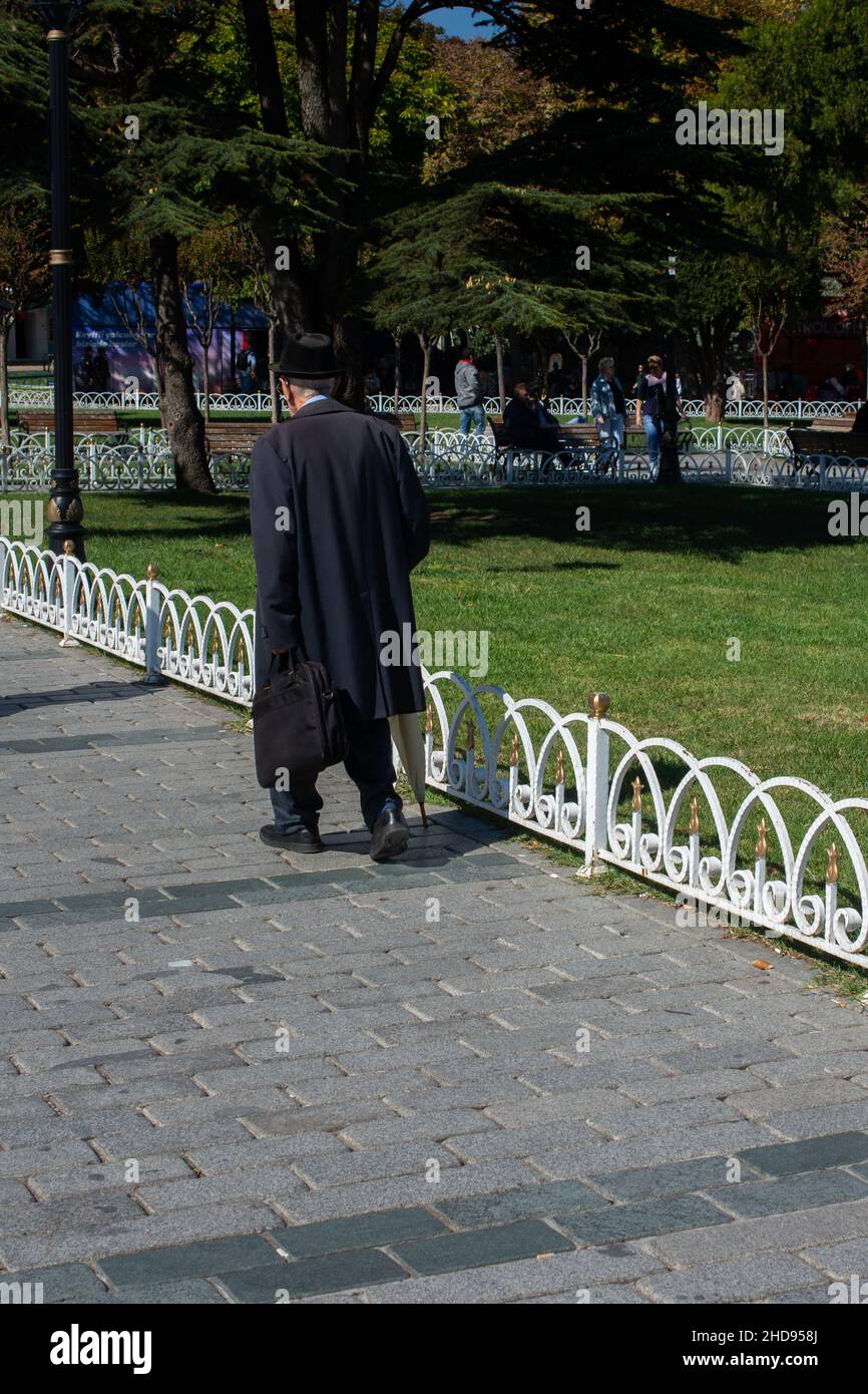 Anciano caminando sobre adoquines cerca de un parque verde Foto de stock