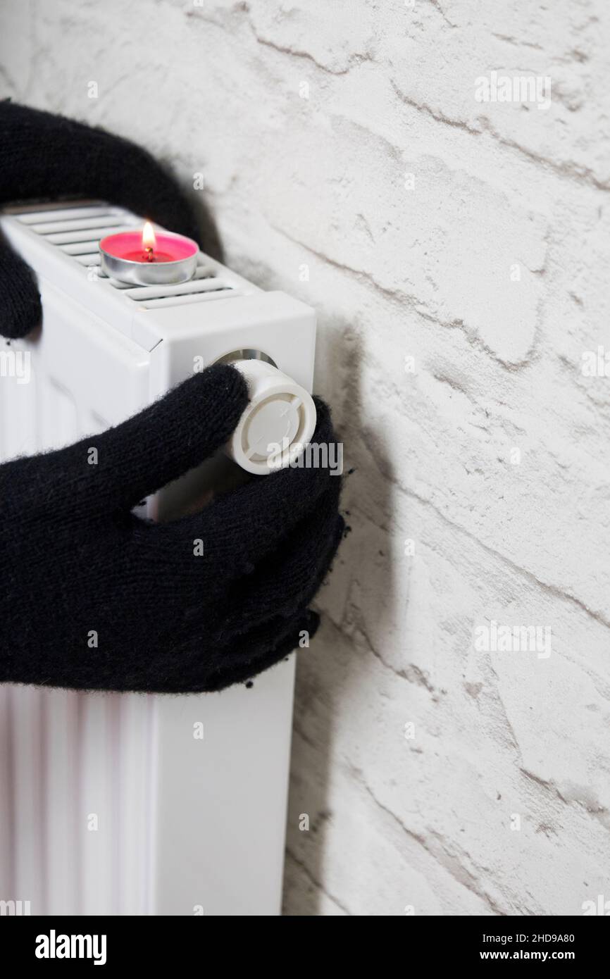 La mano de una mujer en guantes de invierno sostiene el mango del  termostato de calefacción. El concepto del coste de los servicios de  calefacción, el aumento de los precios de la