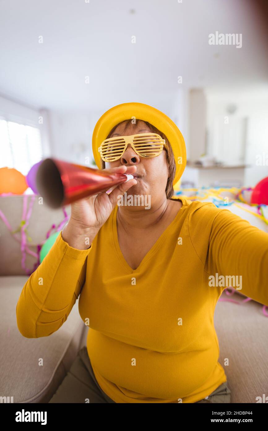 Mujer mayor sin preocupaciones con gafas obturadoras que soplan el cuerno  de la fiesta durante la videollamada en casa Fotografía de stock - Alamy